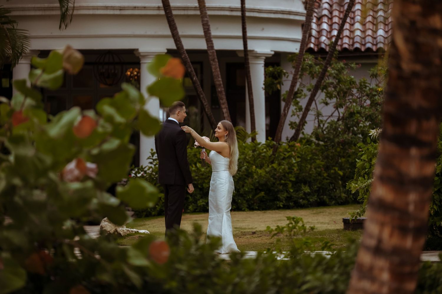 A couple stands together during an intimate outdoor wedding ceremony surrounded by lush greenery and string lights.