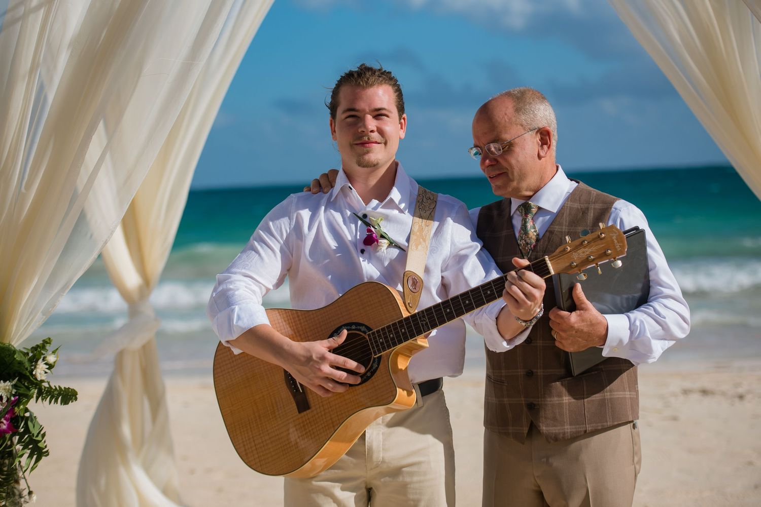 Musicians playing acoustic guitars during beachside wedding ceremony.