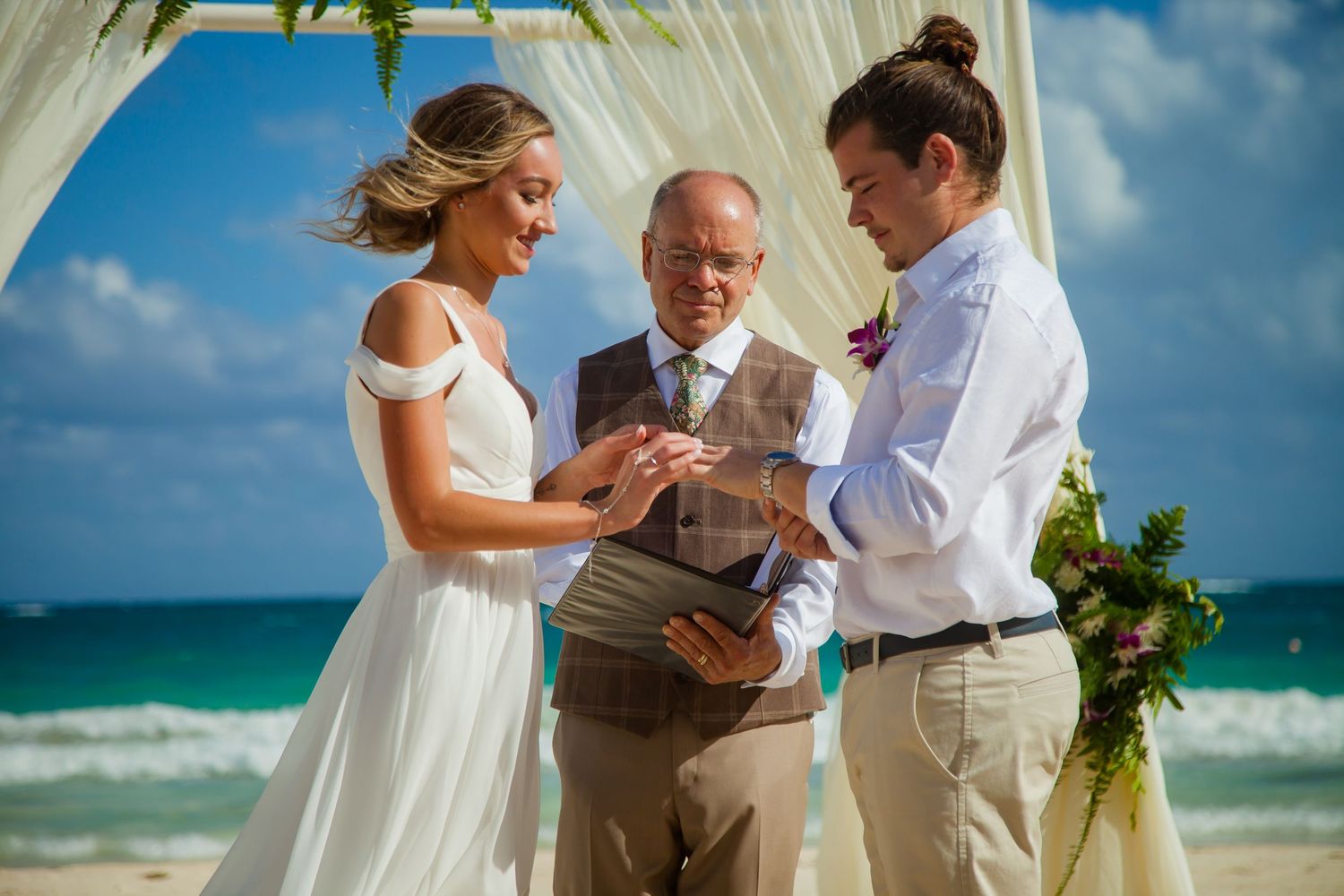 Beachside wedding ceremony with officiant and couple under decorated arch by the ocean.
