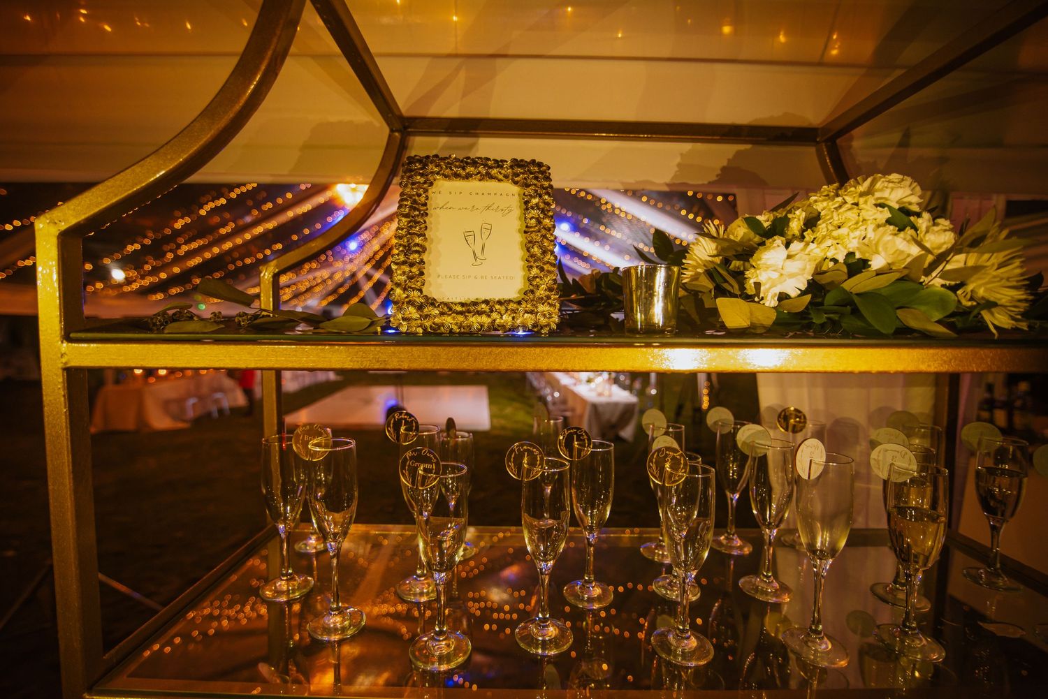 Vintage-style display shelf with glowing candles, glassware and floral decorations at evening event.