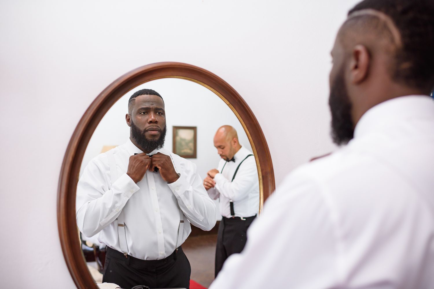 A person adjusting their tie while looking in a mirror during wedding preparations.
