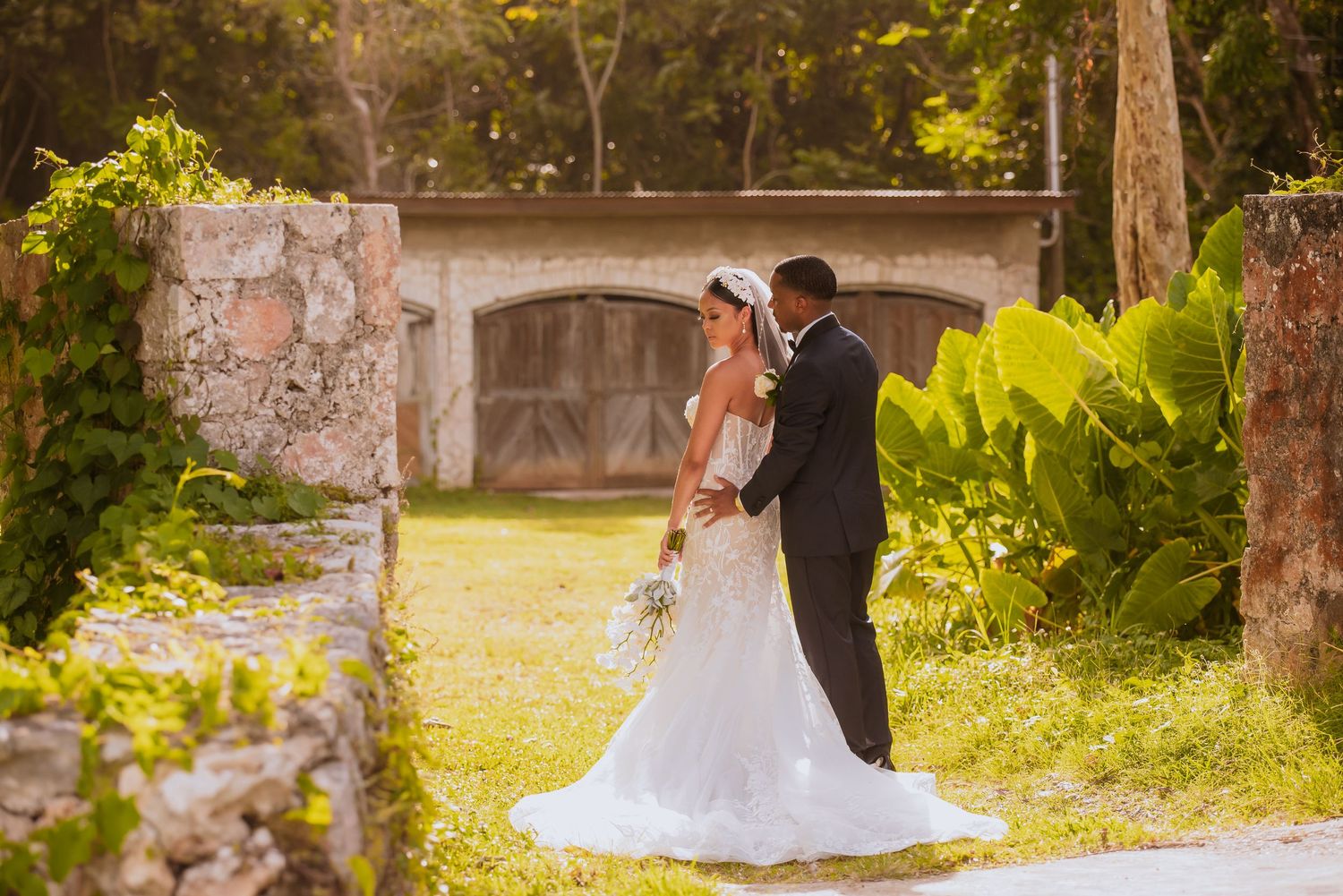 Wedding couple poses against rustic garden walls in warm natural lighting.