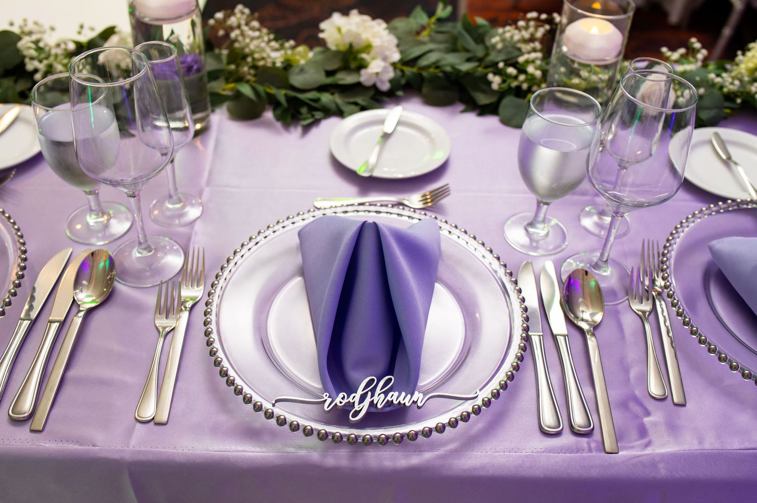 Close-up of formal place settings with purple napkins and silver charger plates.