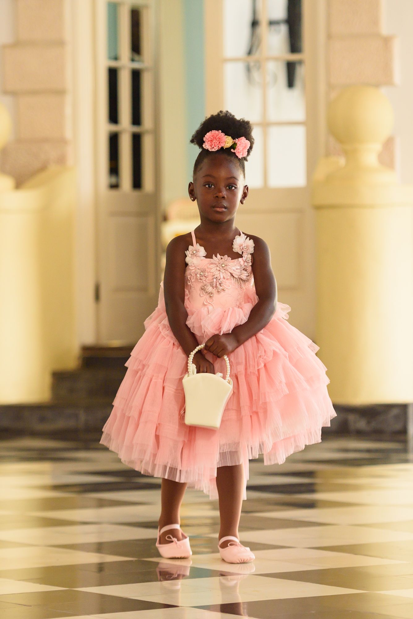 Young flower girl in a pink tulle dress twirling on a checkered floor.