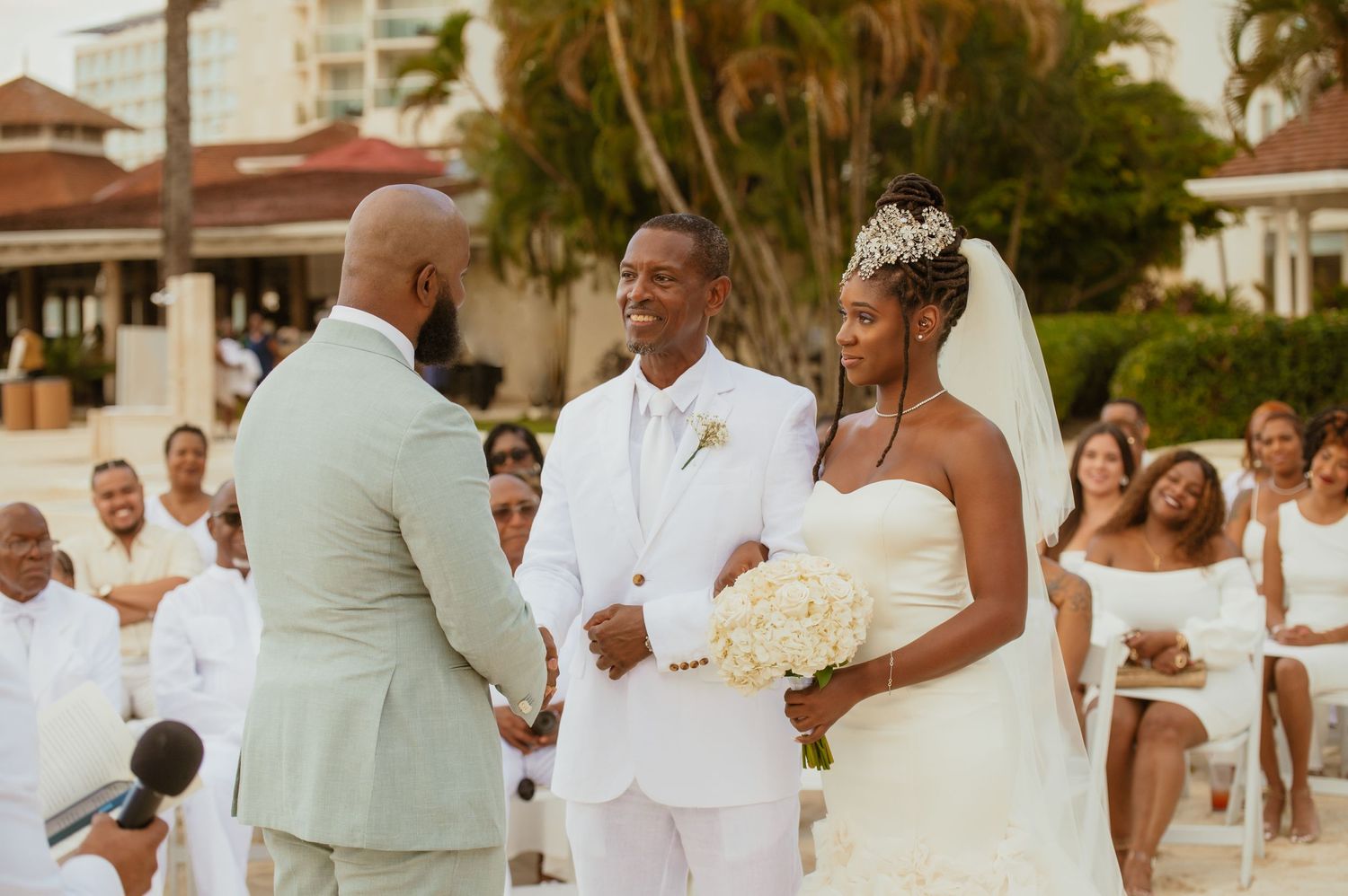 Tropical beach wedding celebration with guests in white and mint green attire.