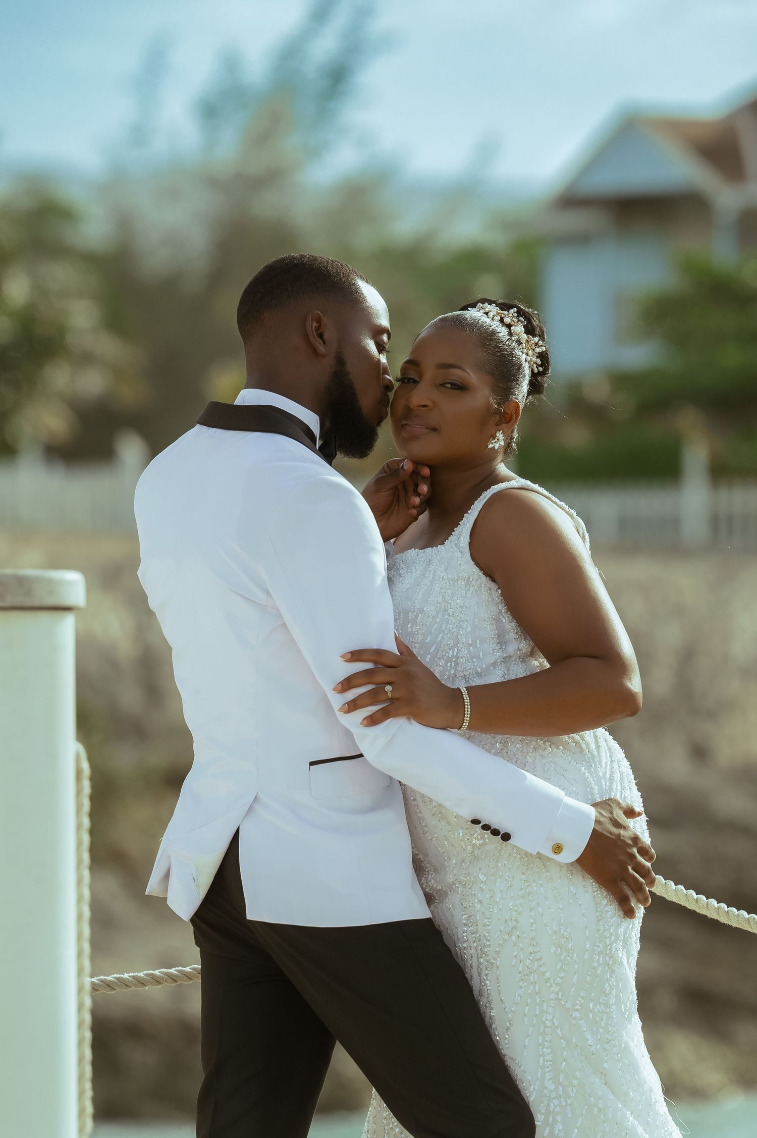 Romantic outdoor wedding photos of couple embracing in white attire.