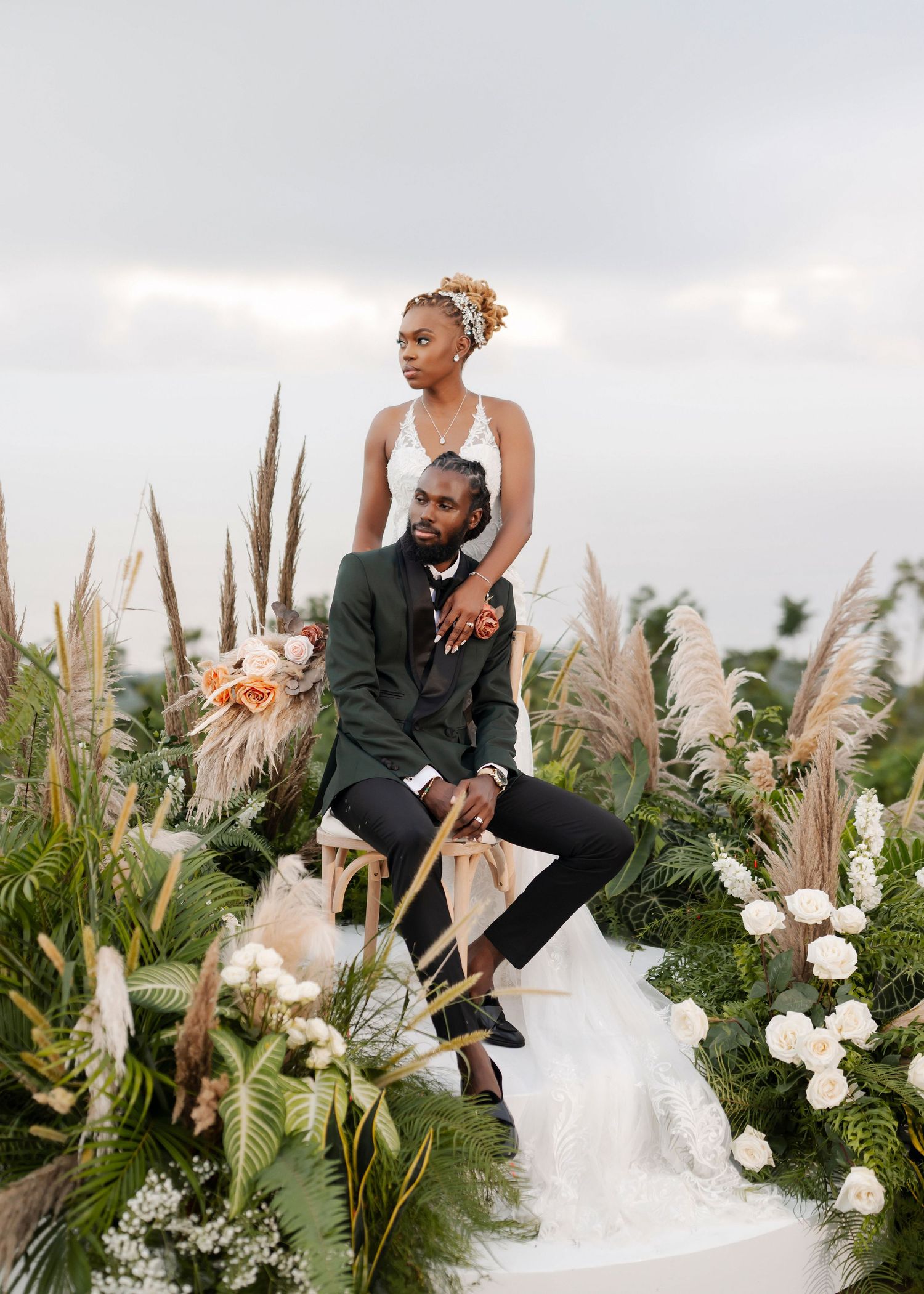 Wedding couple poses dramatically with pampas grass and floral arrangements at outdoor ceremony.