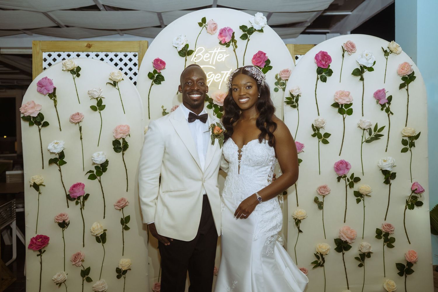 Wedding couple poses against a decorative wall with pink rose patterns.
