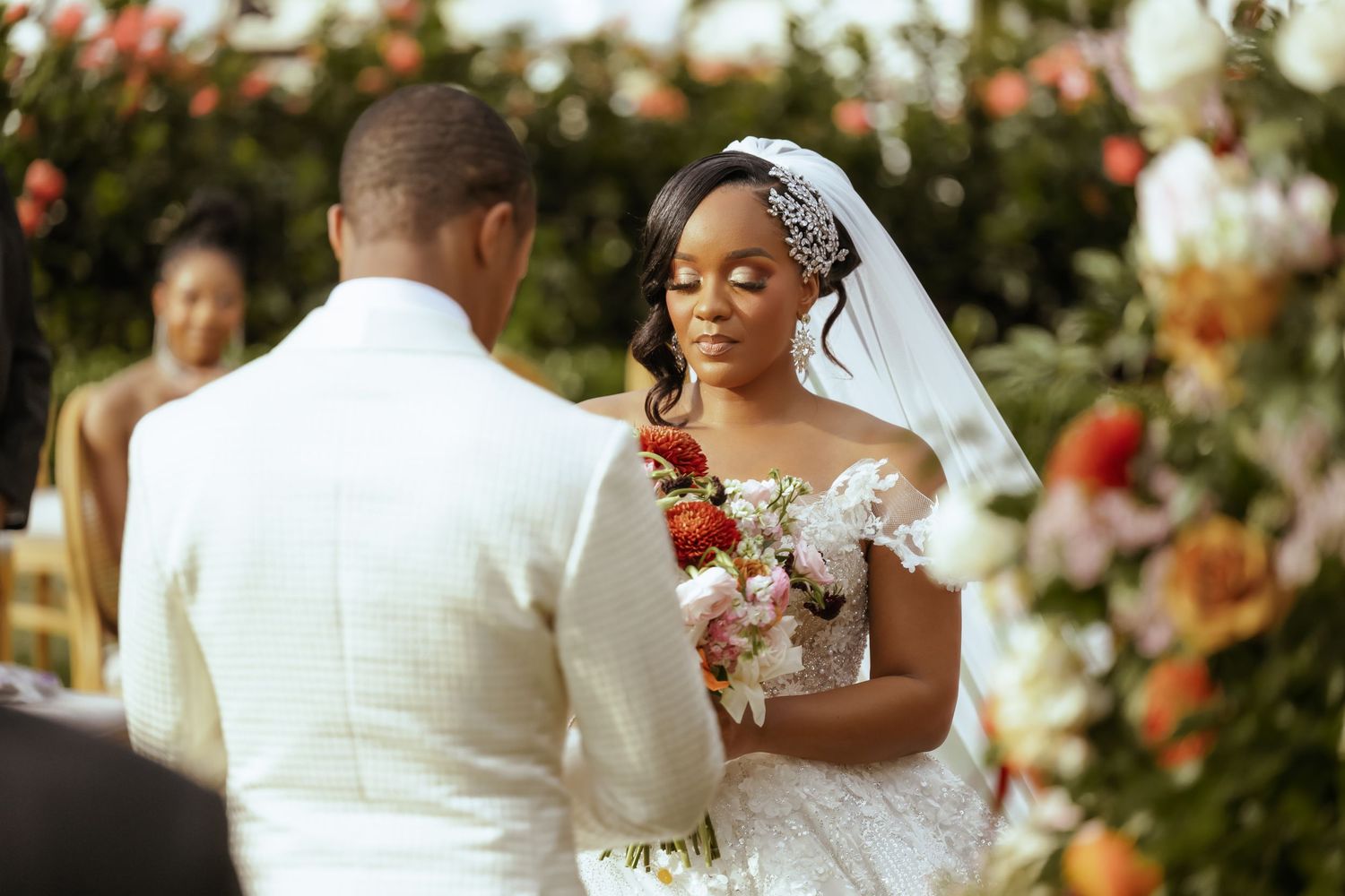 Wedding ceremony setup with floral arrangements and white decor against a bright outdoor backdrop.
