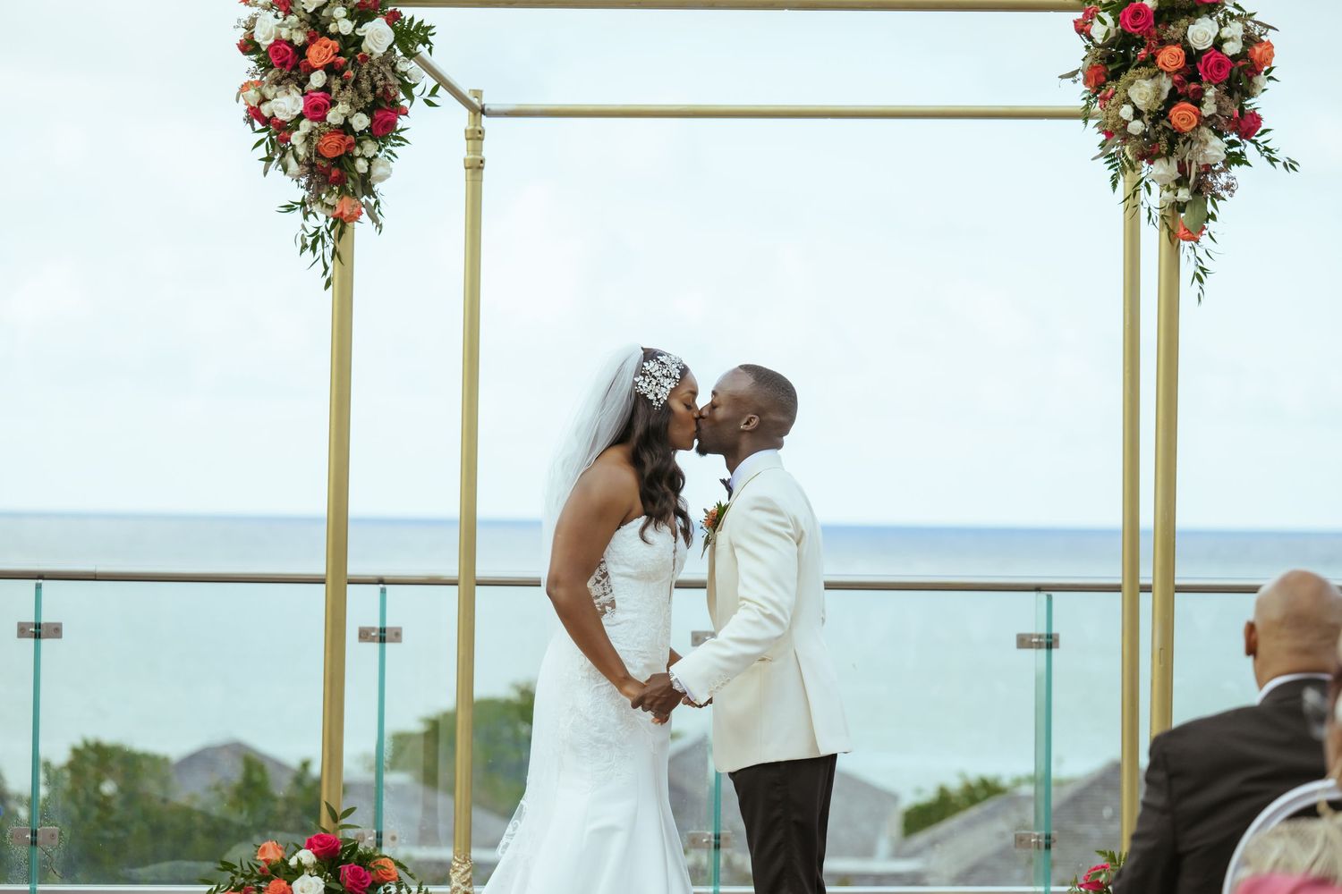 Wedding ceremony setup with gold arch and red floral arrangements on outdoor deck.