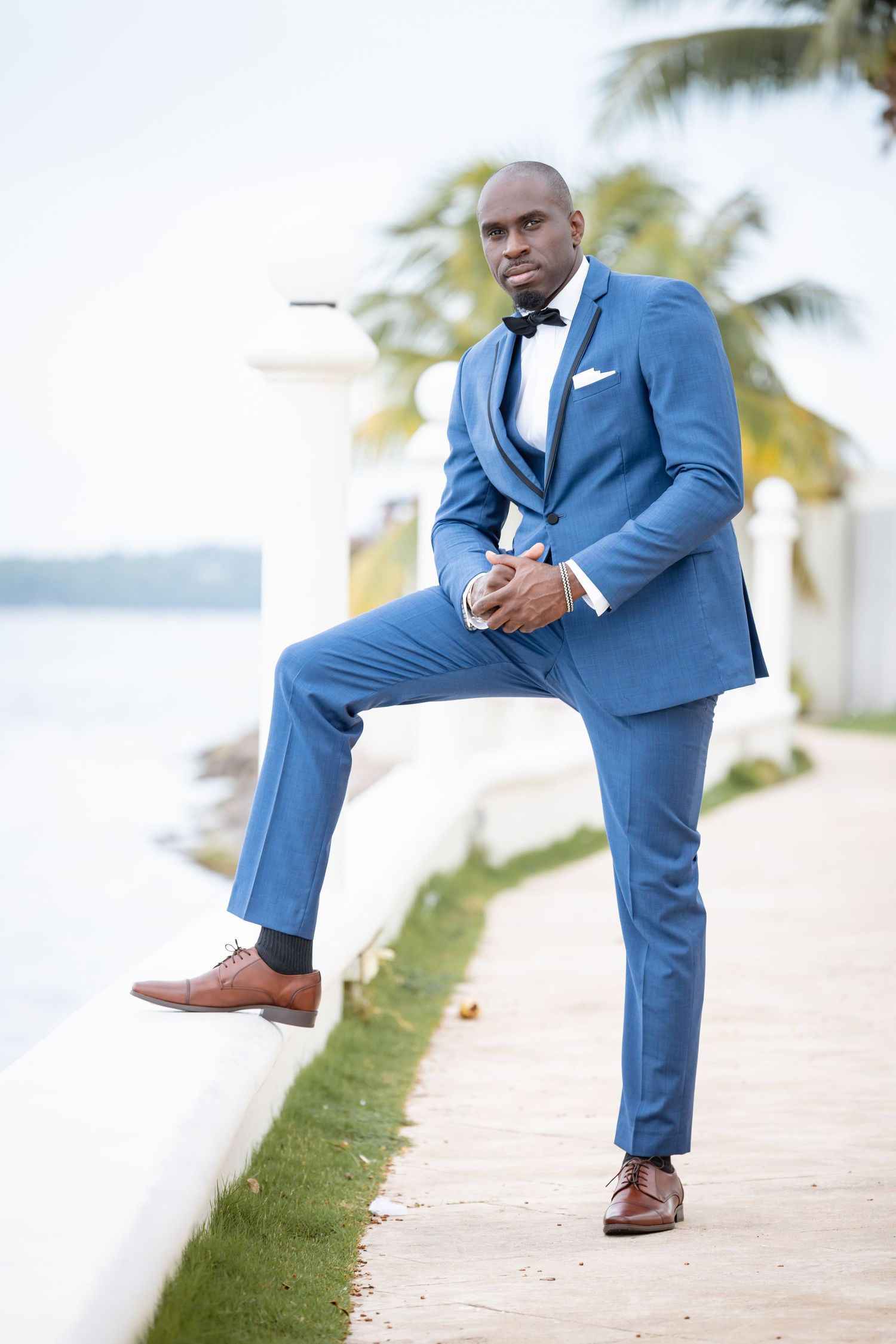 Groom in blue suit strikes dynamic poses against tropical beach backdrop with palm trees.
