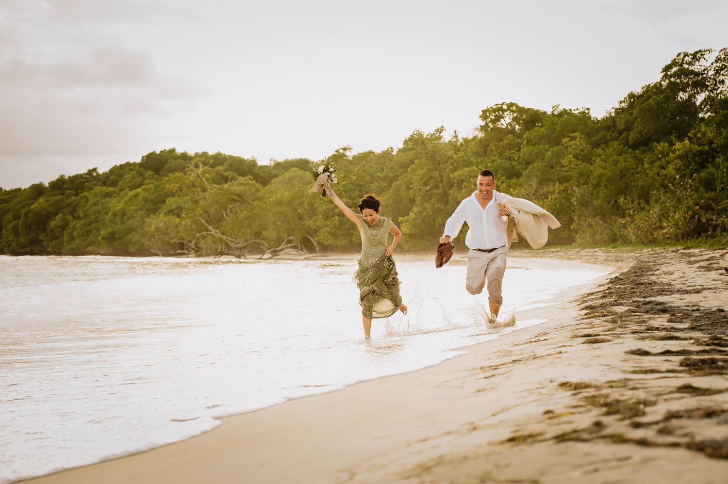 A couple runs playfully along a sandy tropical beach at sunset.