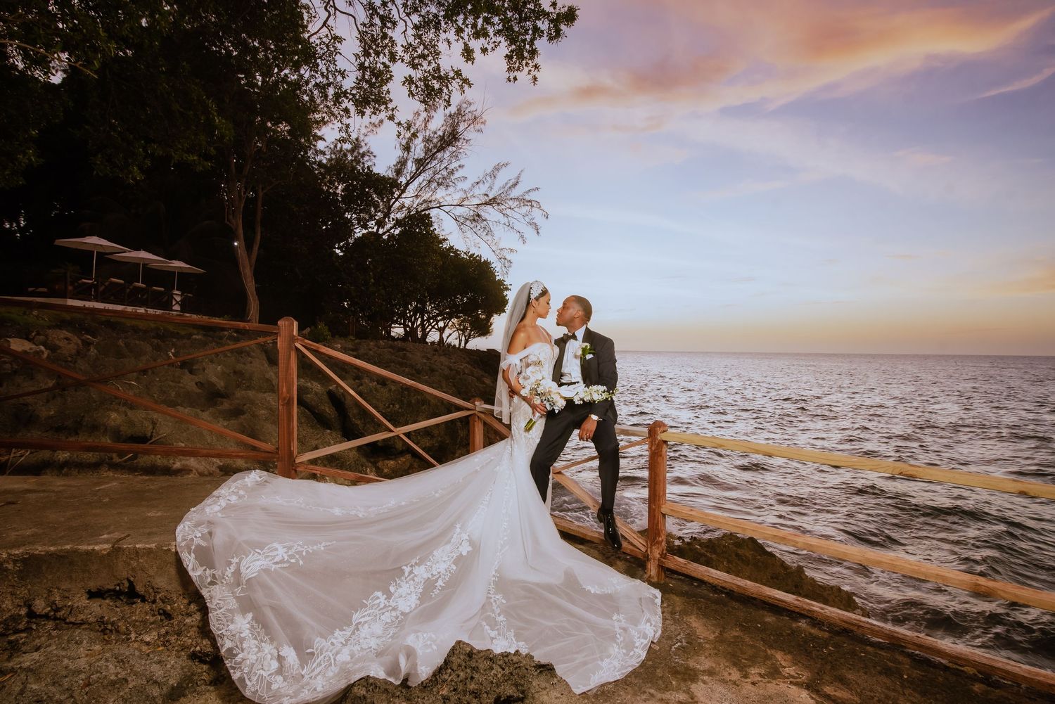 Romantic coastal wedding photos at sunset with wooden railings and ocean backdrop.