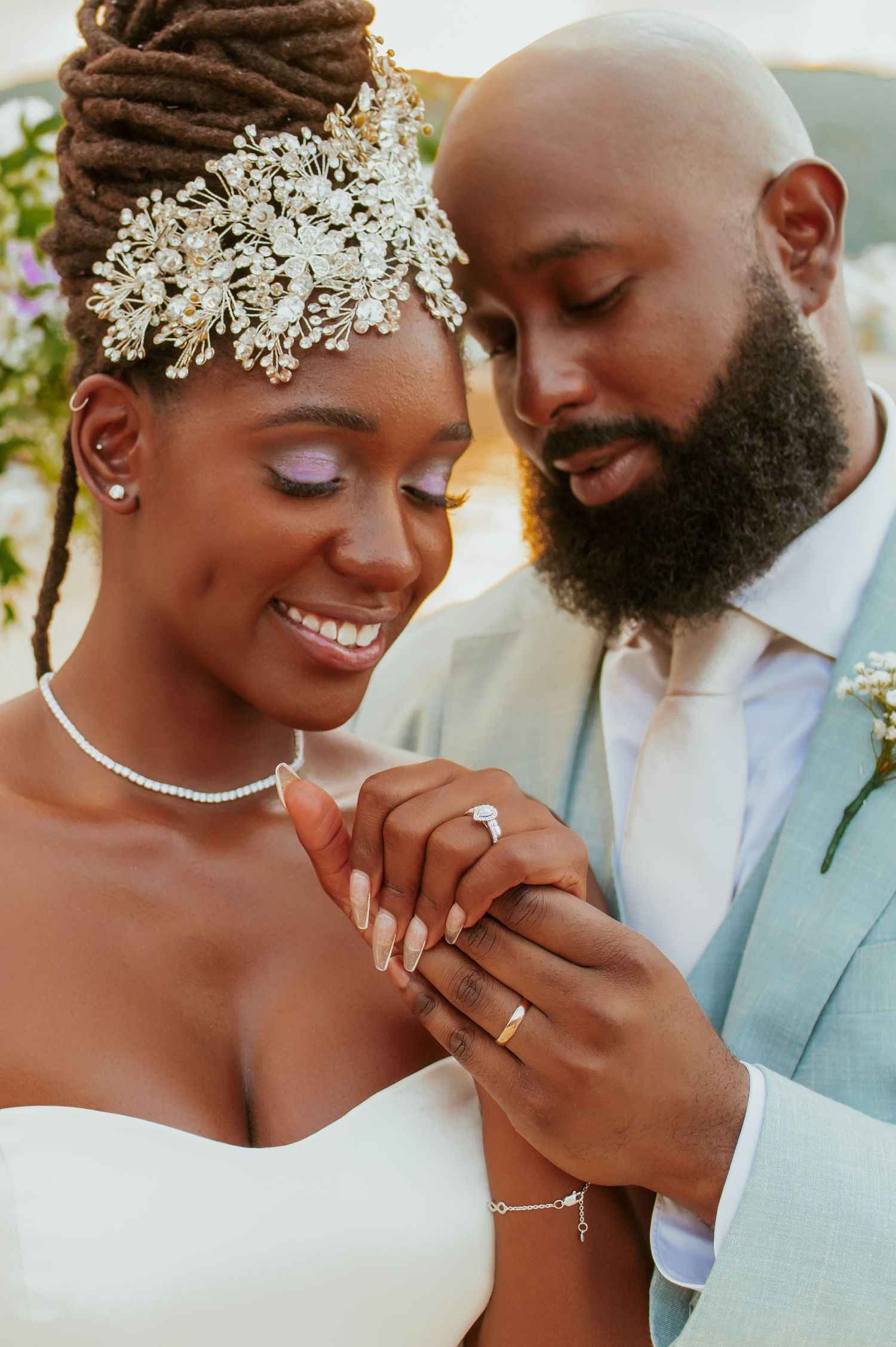 Tender wedding moment captured as couple shares sweet gesture under floral decor on beach.