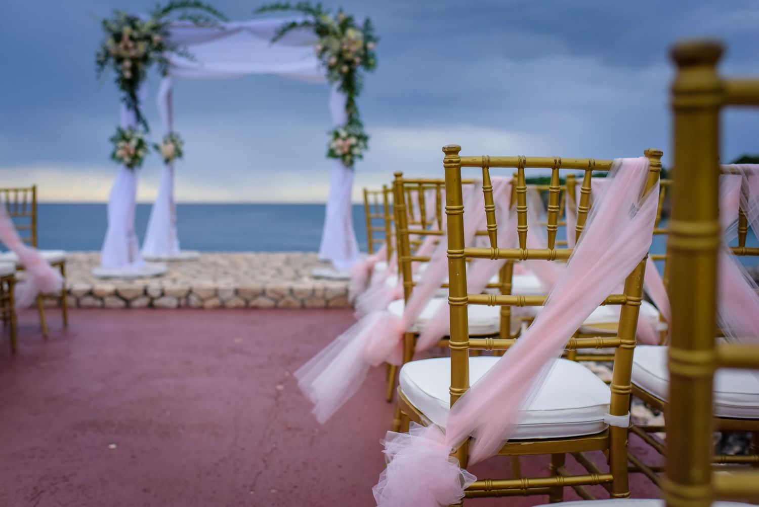 Gold chiavari chairs with pink tulle bows arranged for outdoor wedding ceremony.