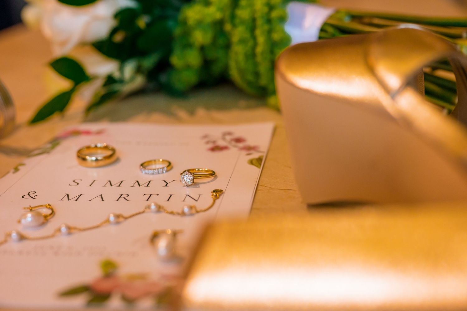 Wedding rings and invitation details captured in warm lighting on a textured surface.
