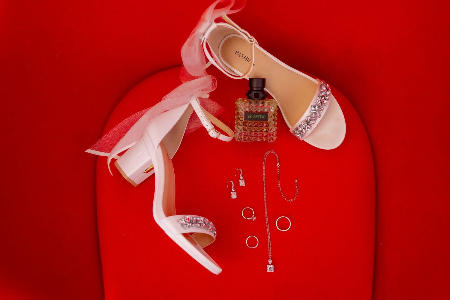 Wedding accessories including white heels and jewelry arranged on red background.