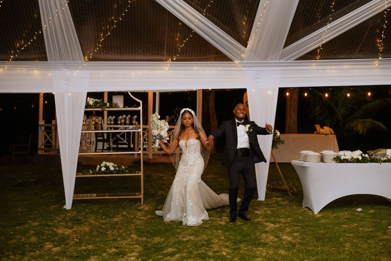 Reception venue with elegant tent setup, display shelves and romantic evening lighting.