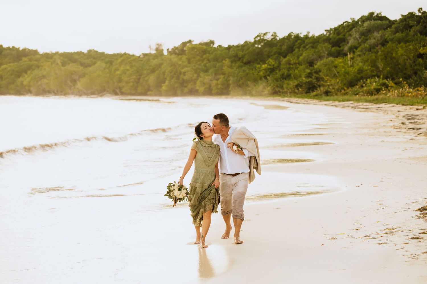 Couple walking hand in hand along pristine white sand beach at sunset.