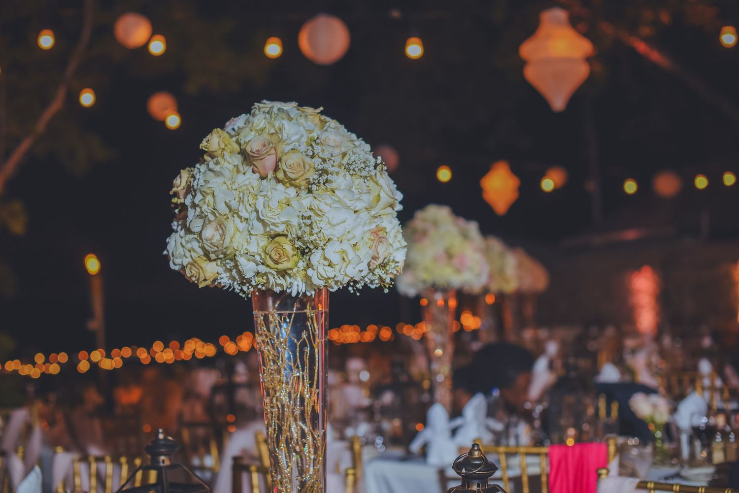 Tall floral centerpieces with white flowers and hanging lights creating an enchanting atmosphere.