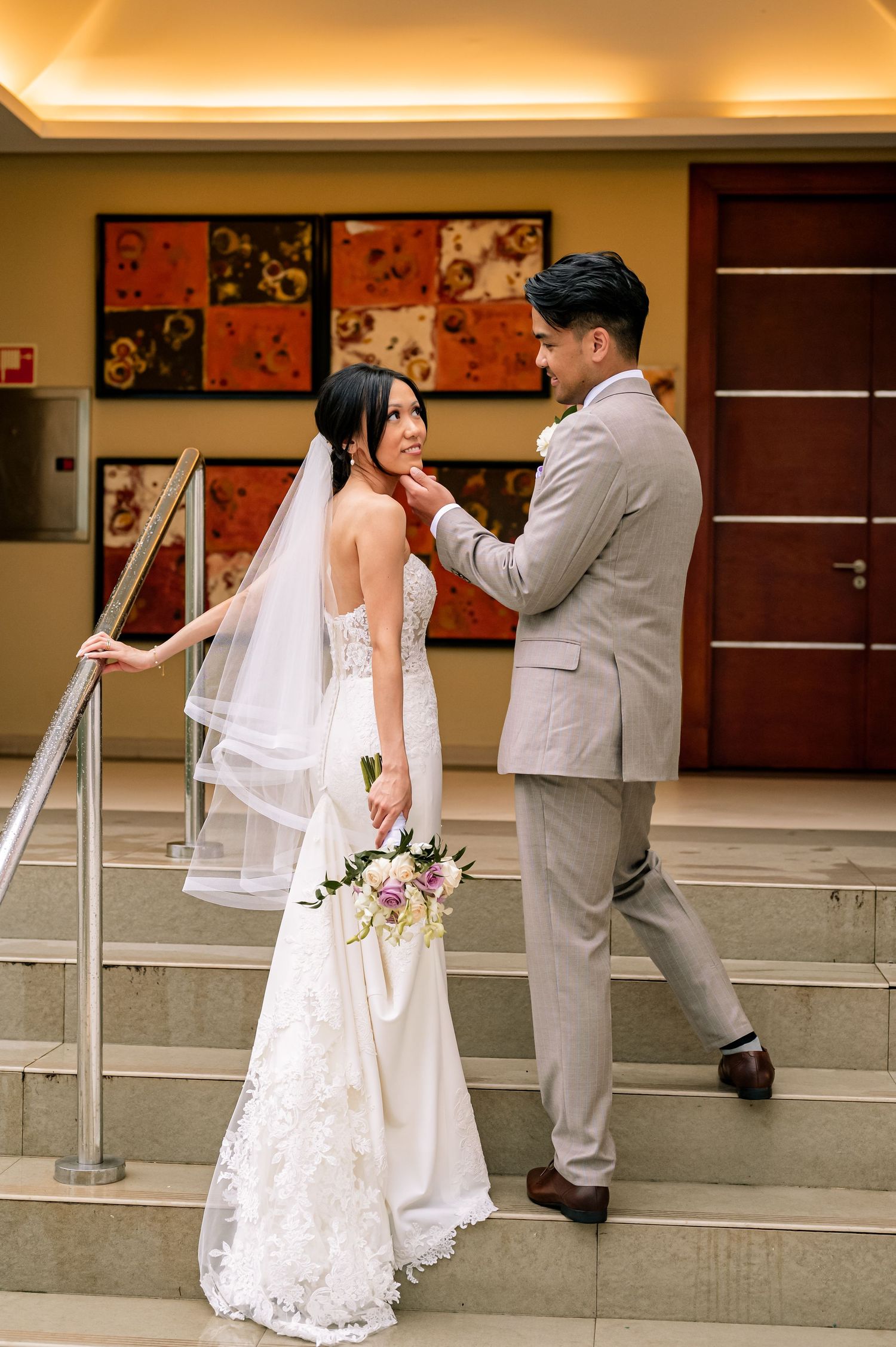 Wedding couple shares tender moments on concrete steps with artistic wall decor in the background.