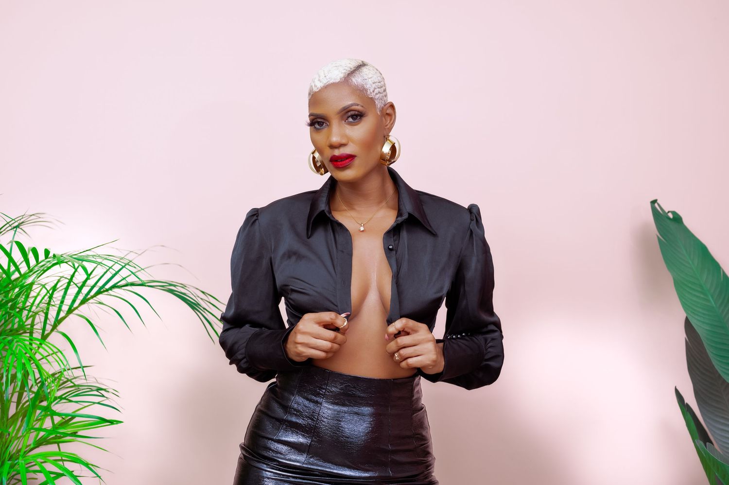 Fashion portrait with black leather jacket against pink background with tropical plants.