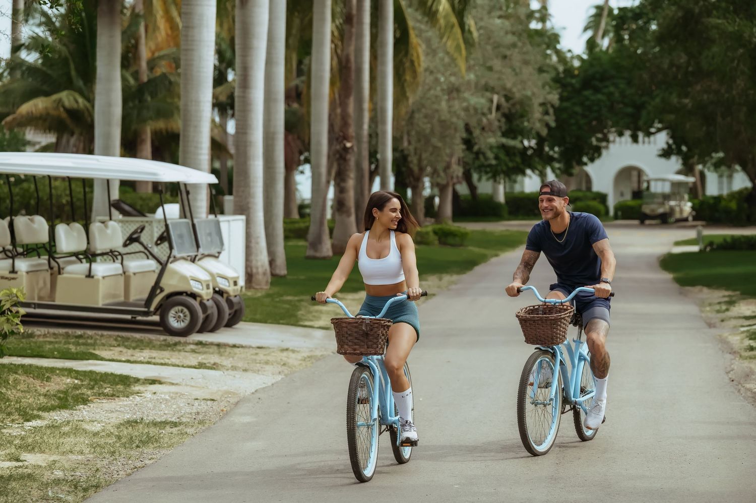 Couple riding blue bicycles together down a palm tree-lined street.