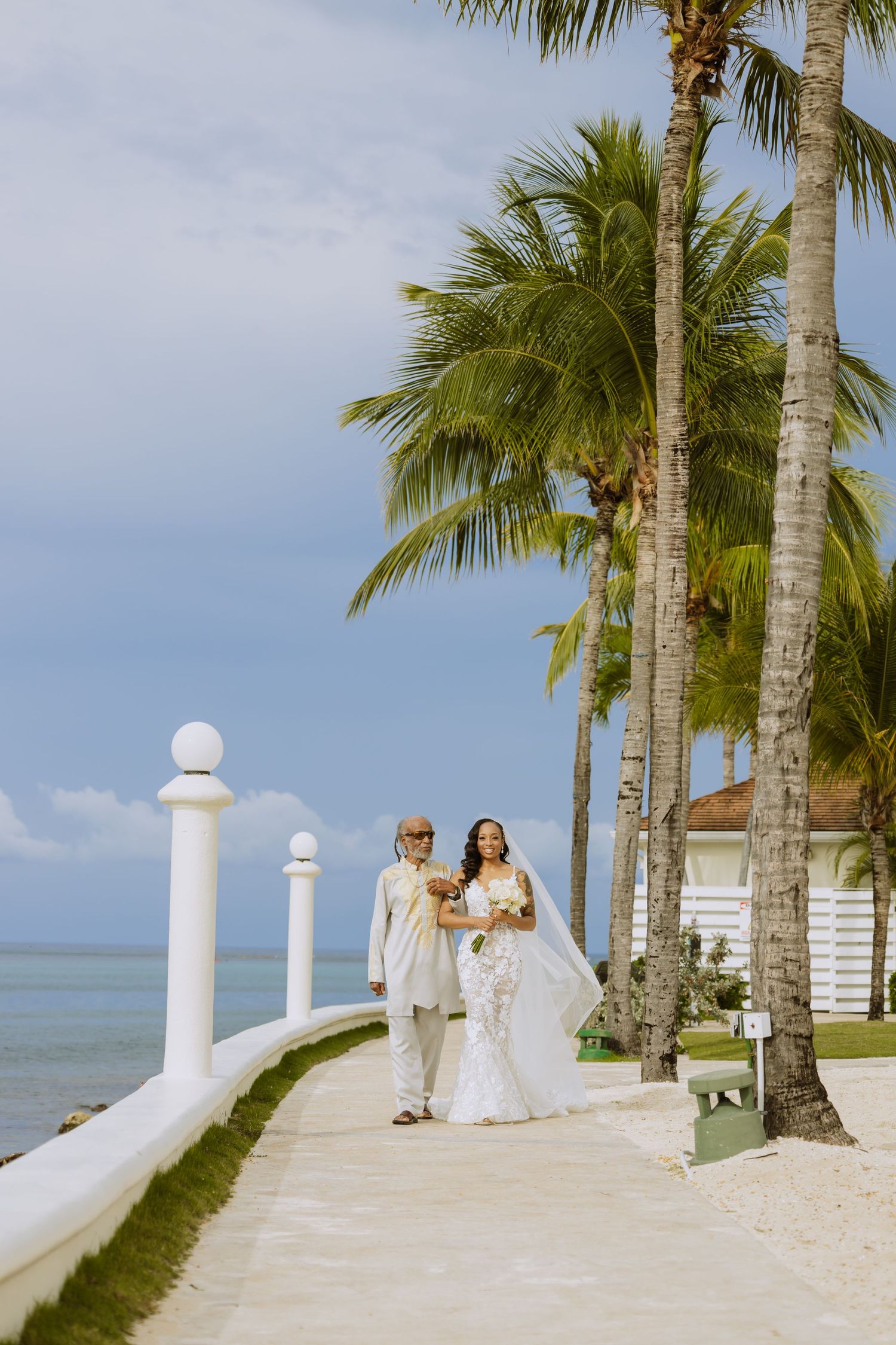 Scenic beach wedding setting with white railings and palm trees along oceanfront path.