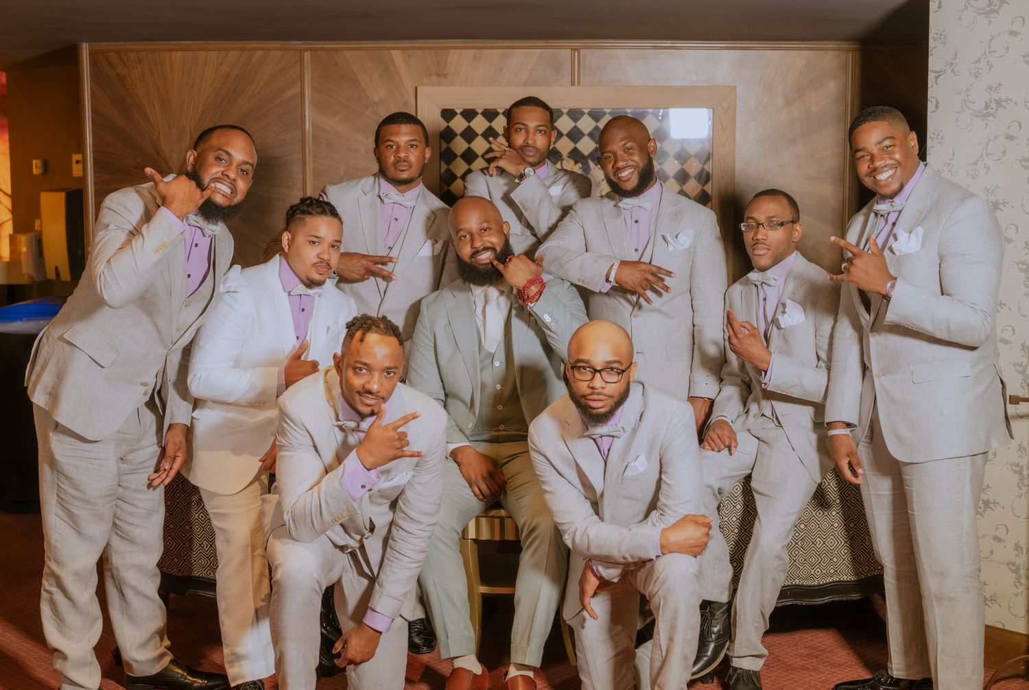 Large wedding party in matching gray suits posing together for group photo.