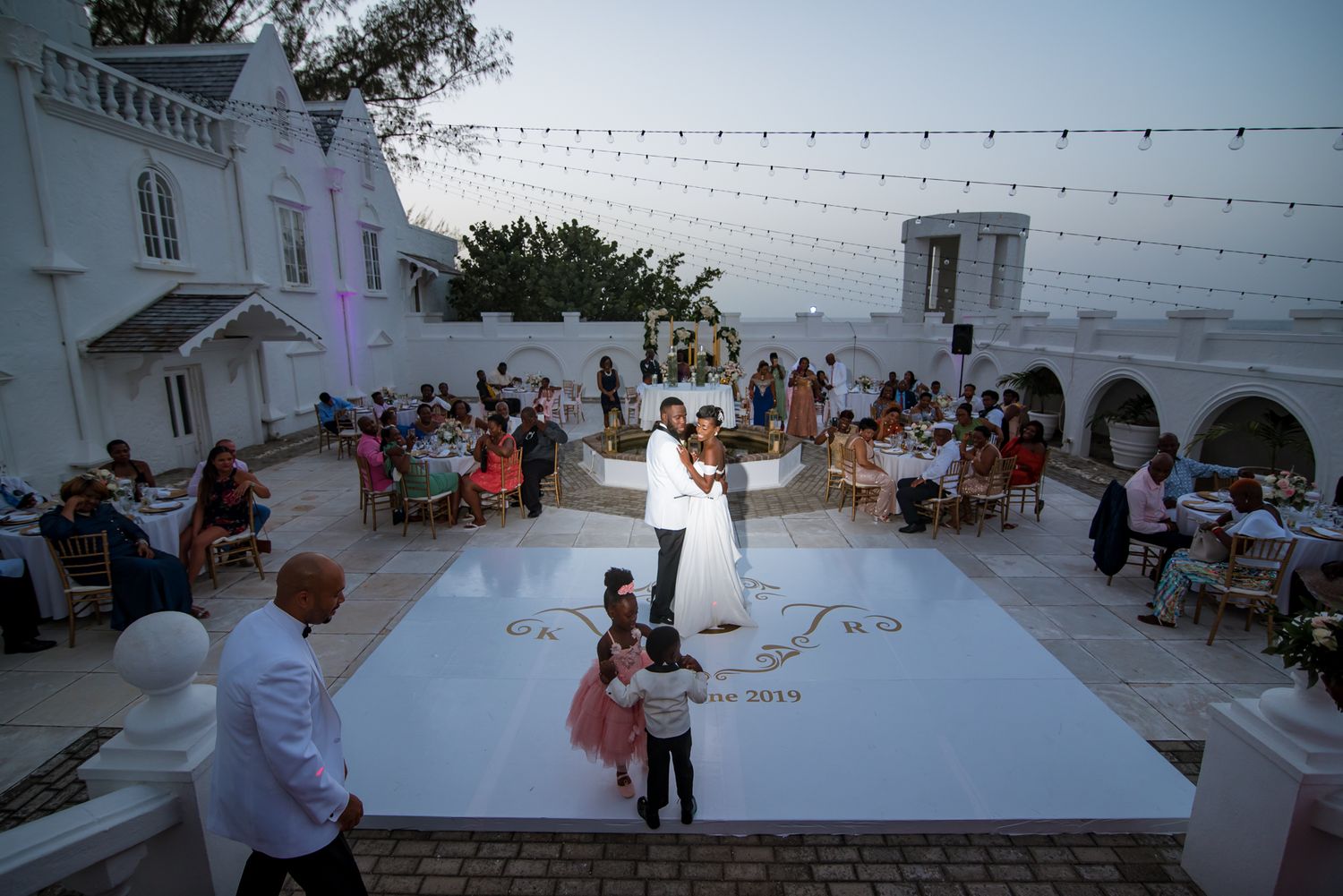Outdoor wedding reception venue with string lights and white decor at sunset.