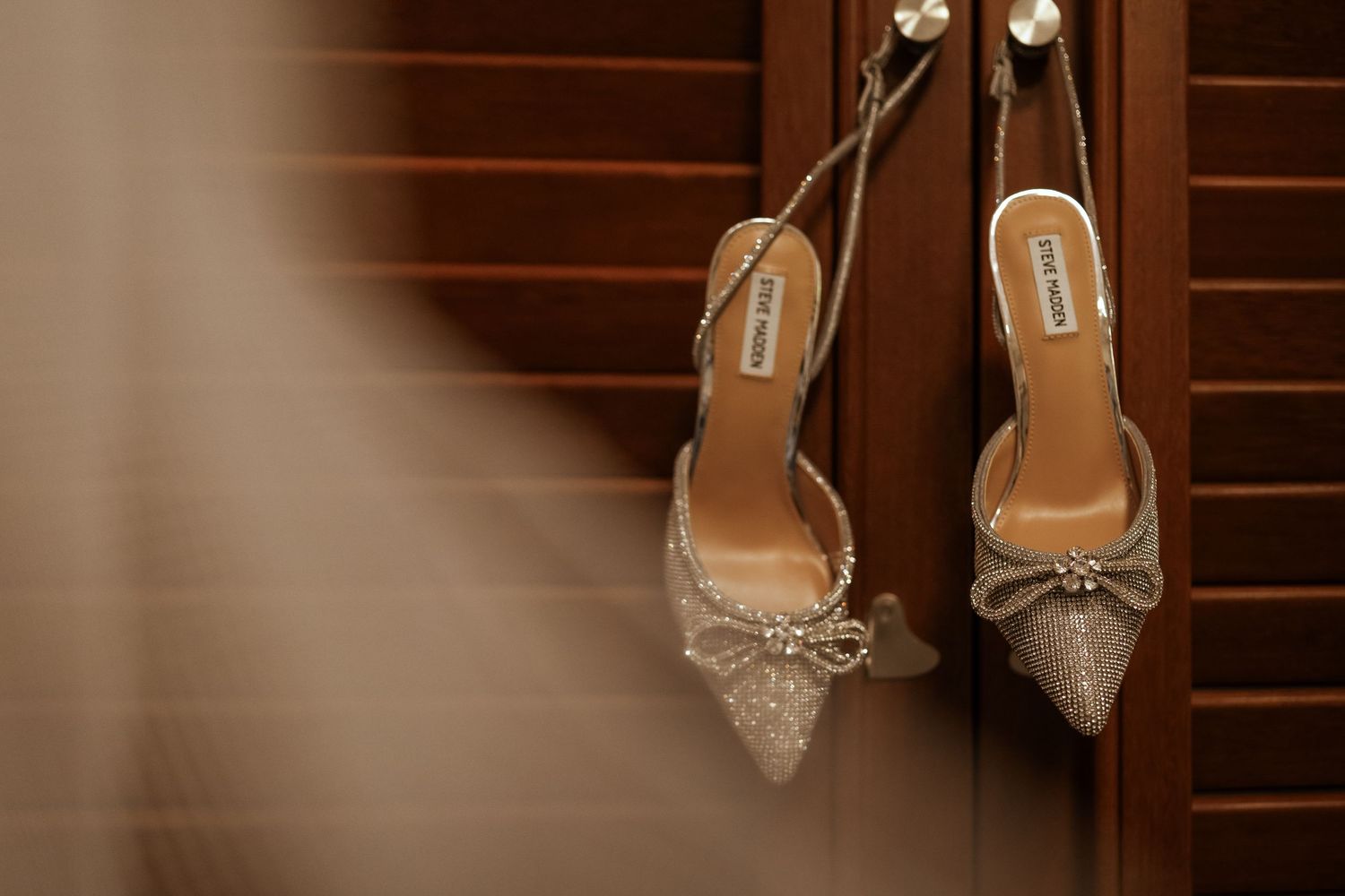 Row of elegant crystal-embellished bridal shoes displayed on wooden shelves.