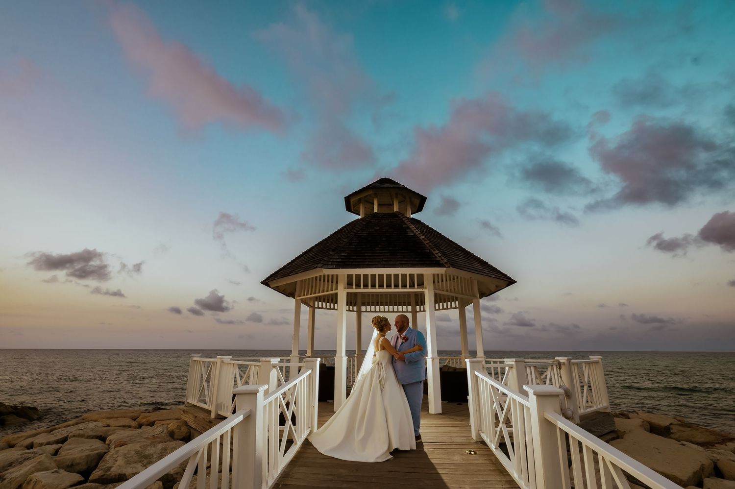 Sunset wedding ceremony at a beachfront gazebo with dramatic sky and ocean views.