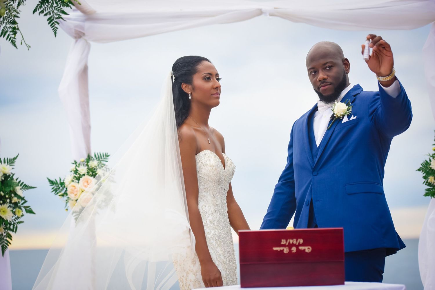 A couple exchanges vows during an outdoor wedding ceremony under a floral arch by the ocean.