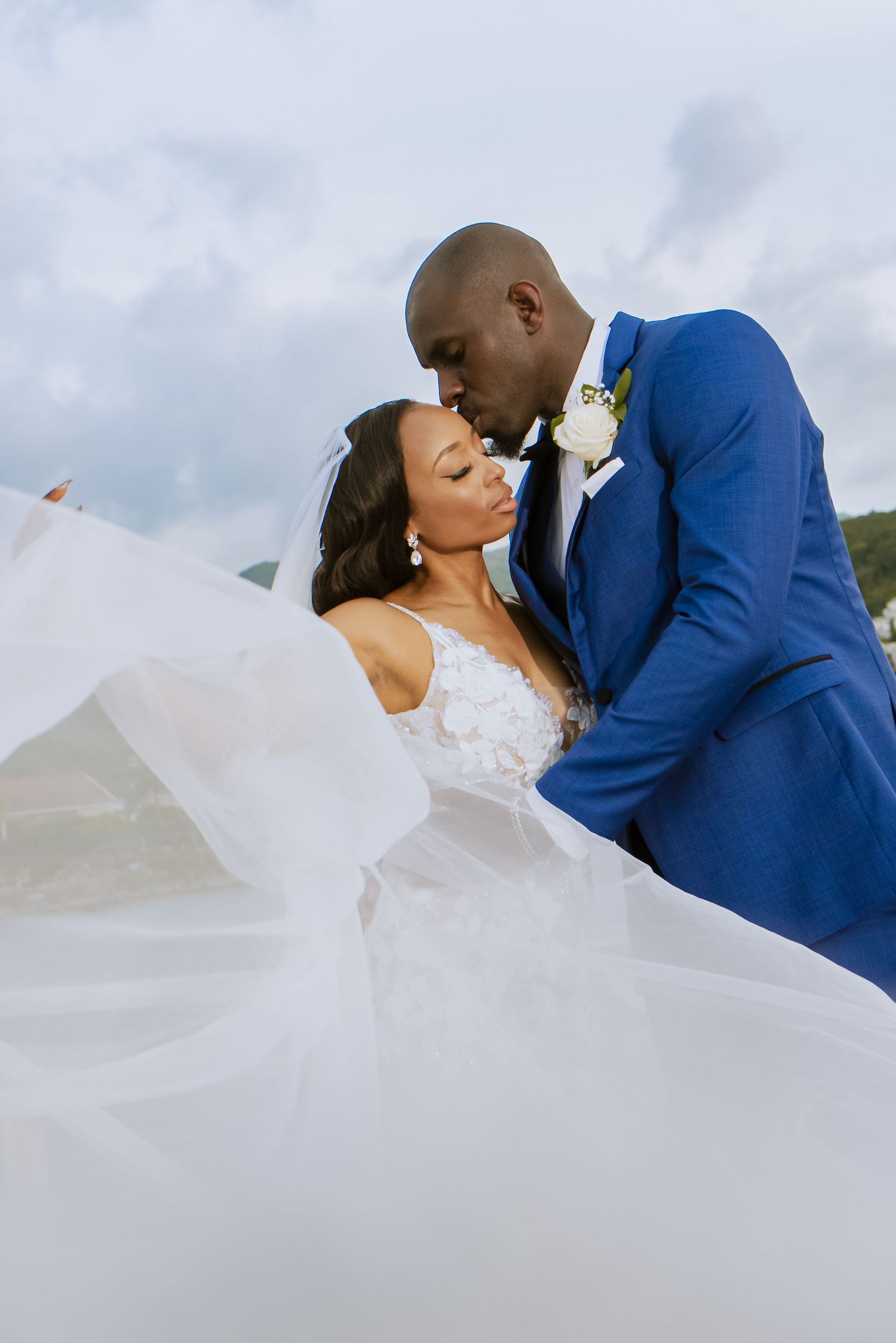 Bride's flowing veil creates dramatic effect during romantic waterfront wedding photoshoot.