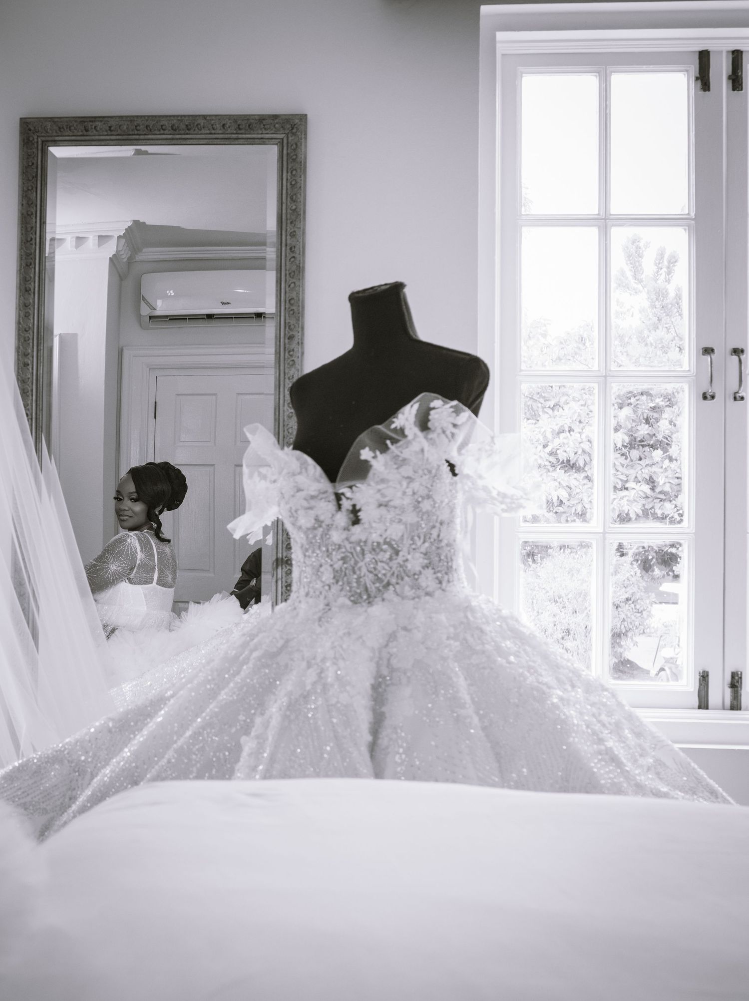 Multiple white wedding dresses hanging on display in a bright sunlit room with windows.