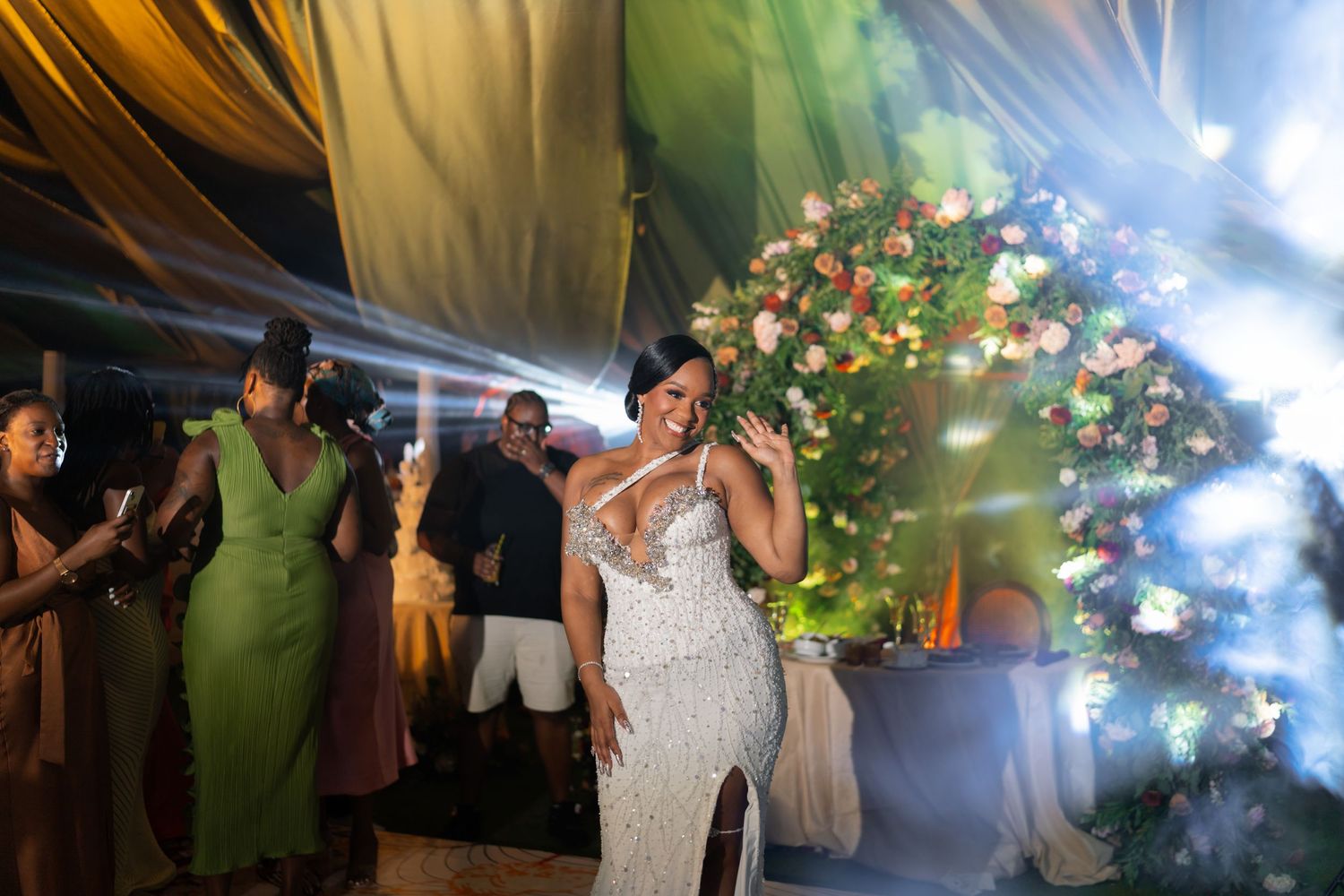 Wedding celebration under tent with dramatic lighting and floral decorations.