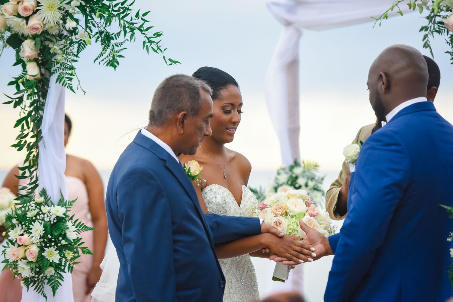 Wedding ceremony participants share an emotional moment under an elegant floral arch with white draping.