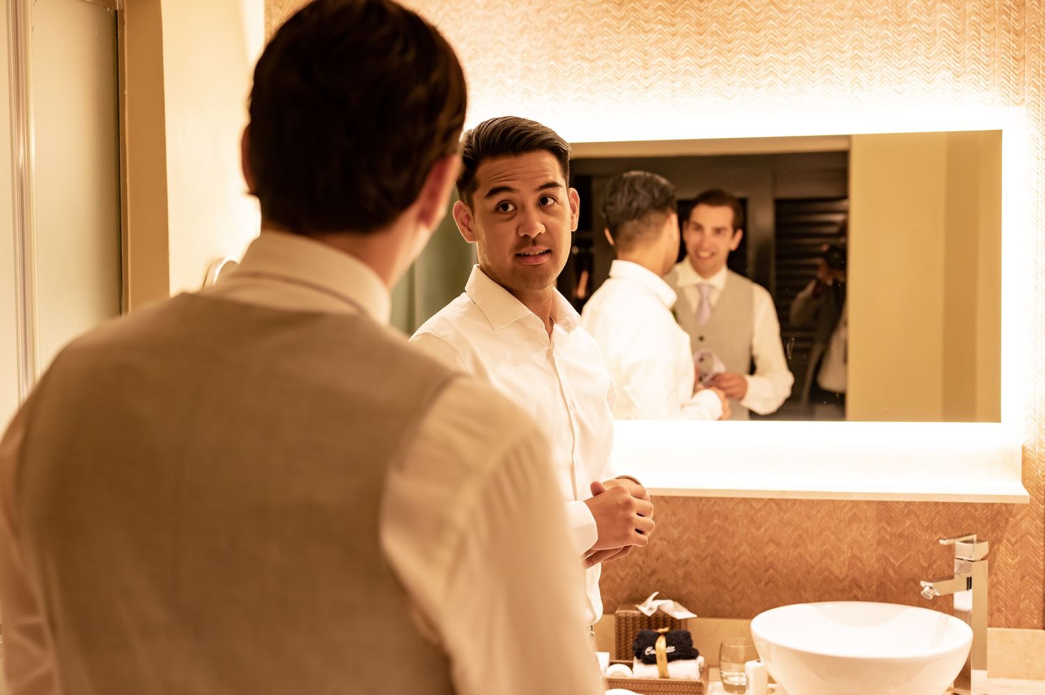 Reflections in bathroom mirror show wedding preparation scene with warm lighting.