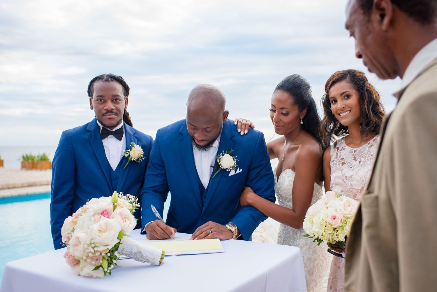 Wedding ceremony participants signing documents at an outdoor beach celebration.