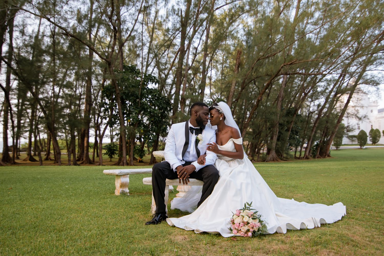 Newlyweds pose for romantic portraits on a scenic grassy lawn with trees in the background.