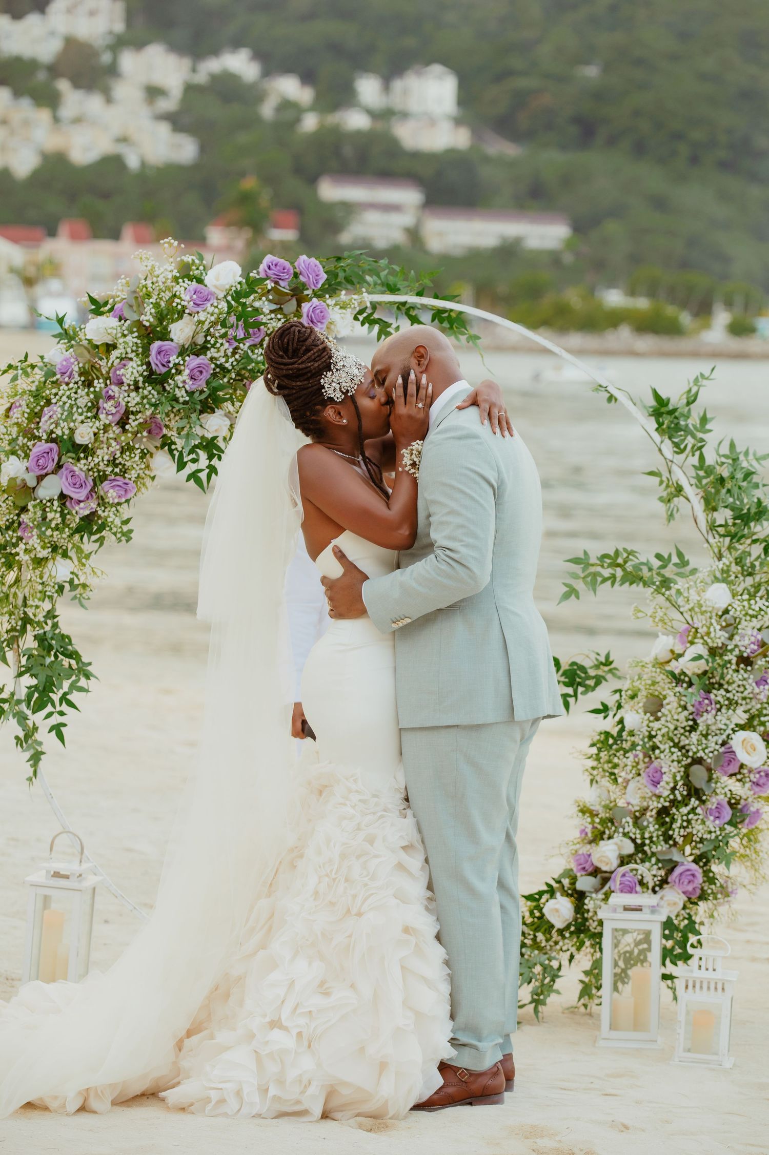 Romantic beach wedding scene with couple kissing under a floral arch by the ocean.