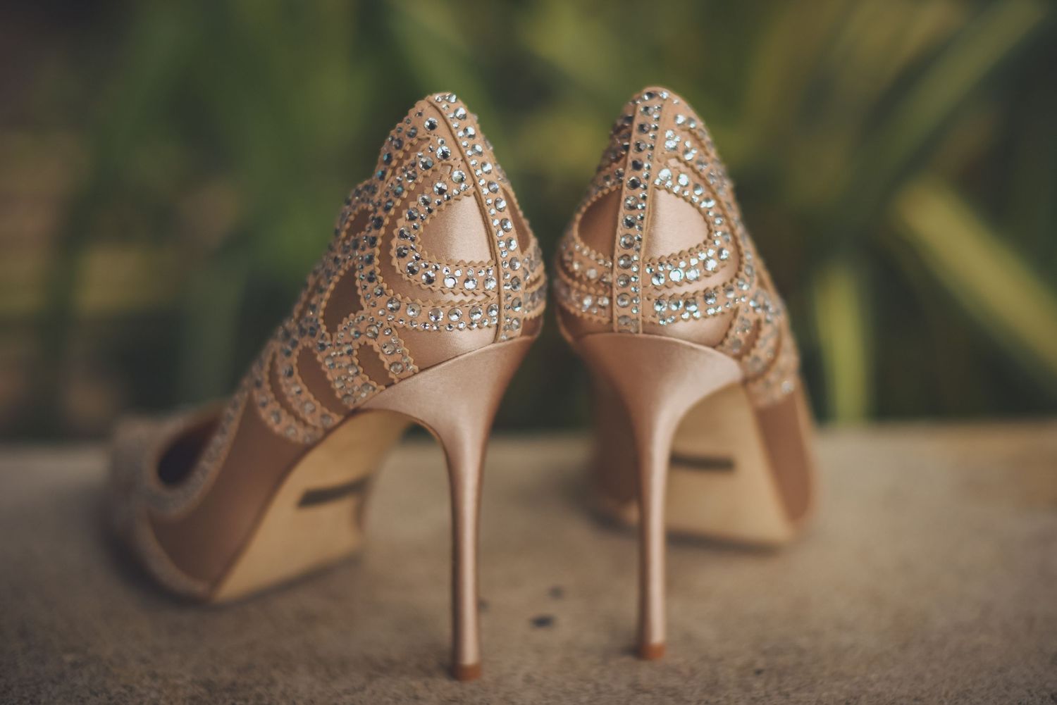 Elegant nude-colored bridal heels with crystal details displayed outdoors.
