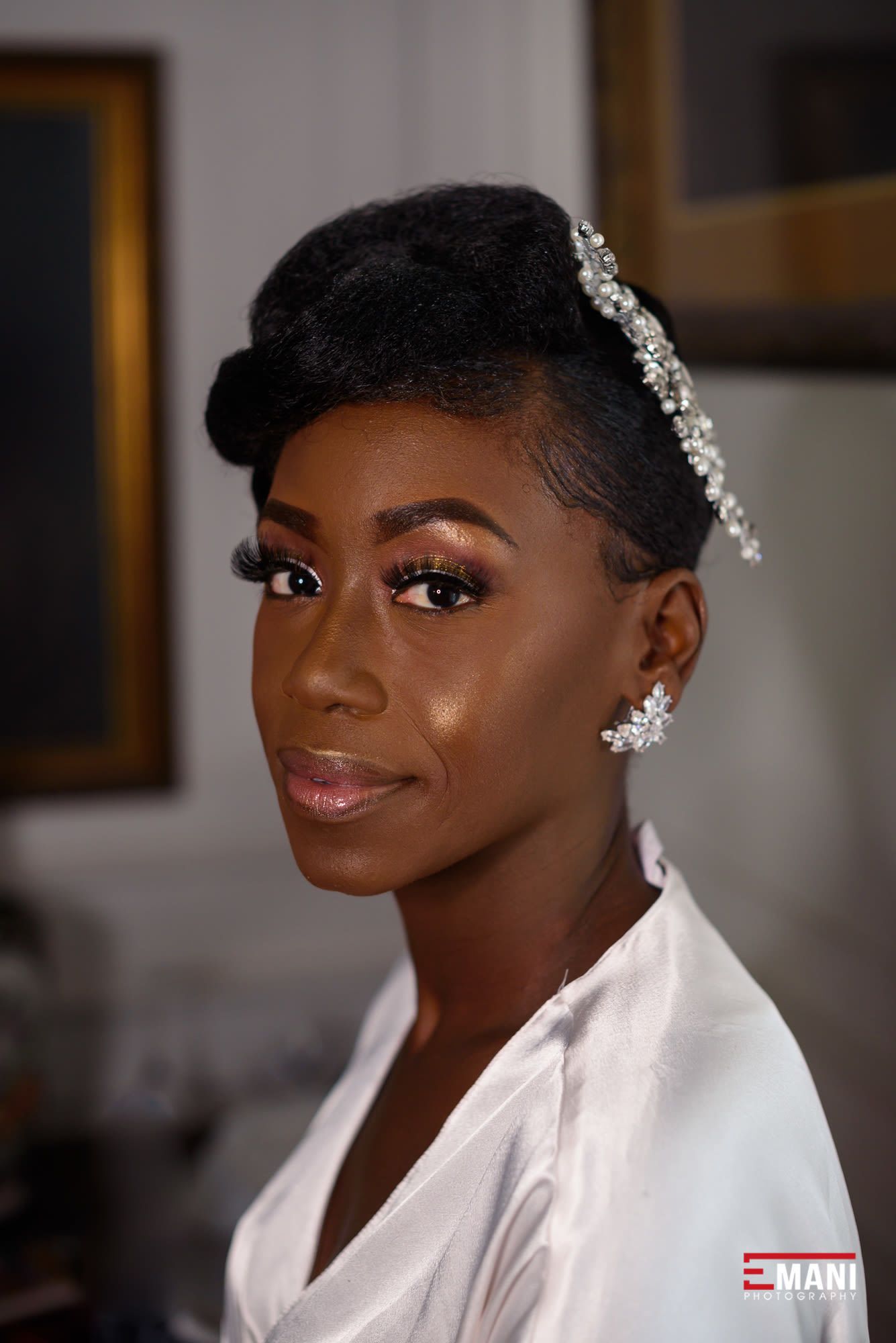 A bride wearing a white robe and crystal hairpiece smiles during wedding preparations.