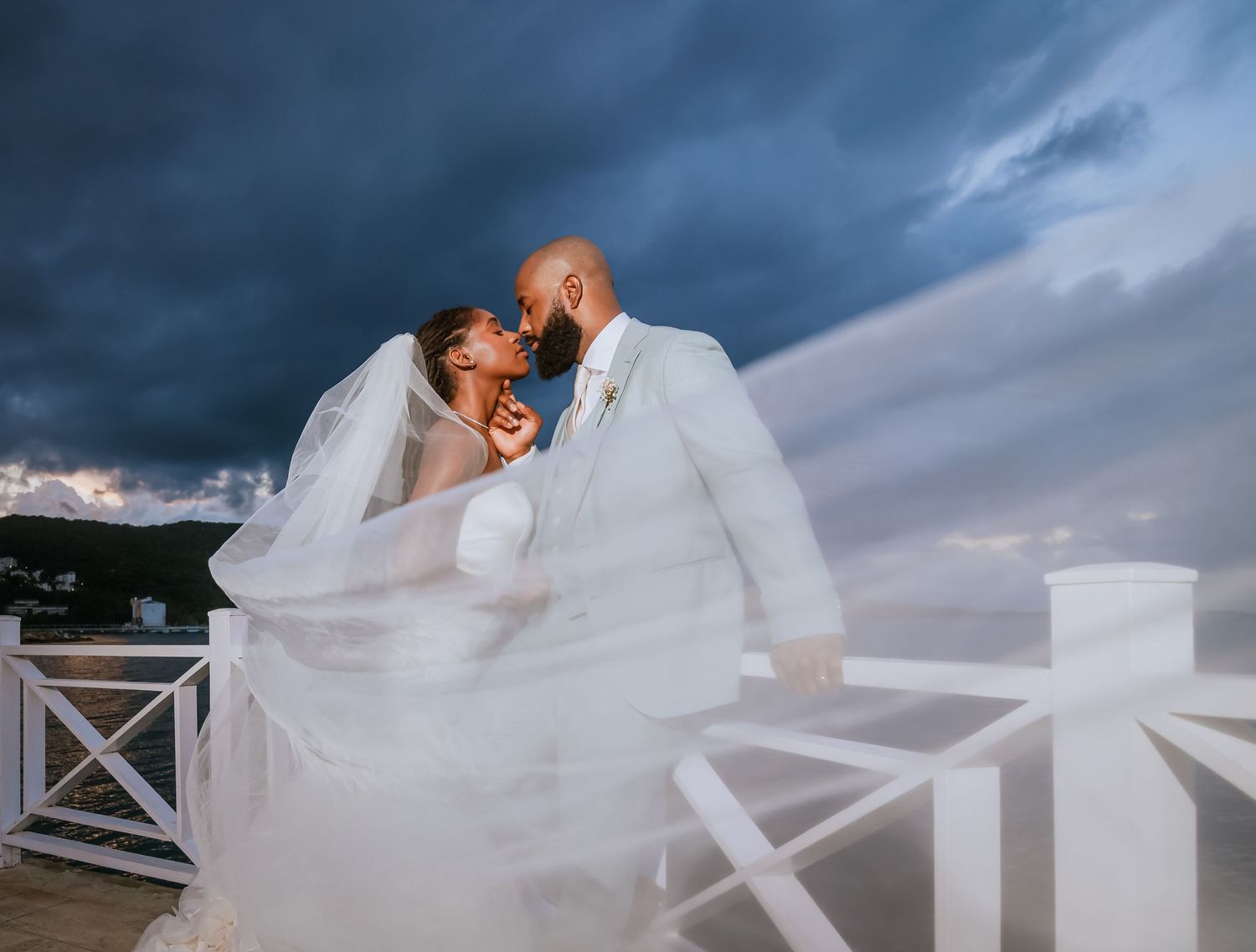 A dramatic wedding photoshoot with flowing veil against a stormy blue sky.