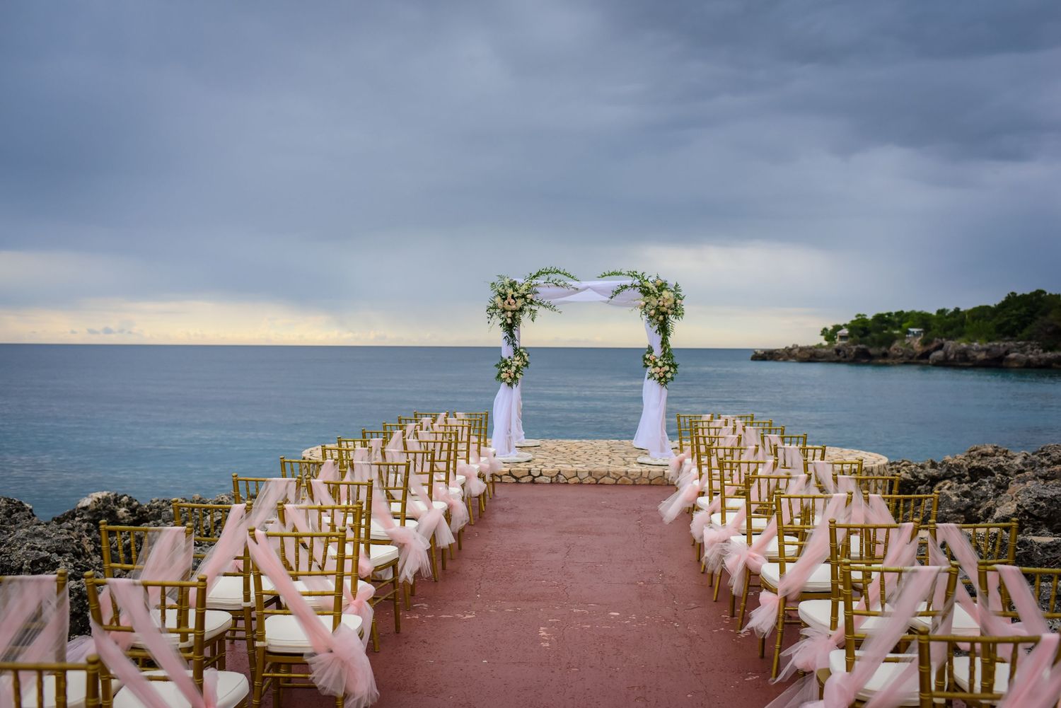 Panoramic view of wedding ceremony setup on oceanfront terrace with decorated chairs.