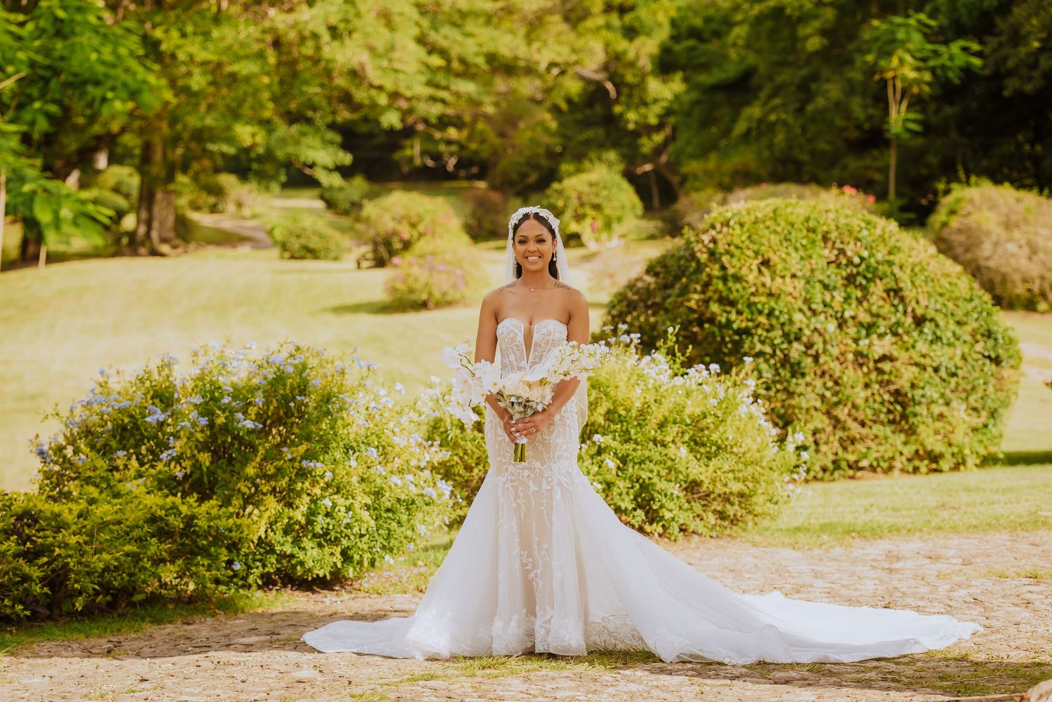 A stunning white wedding dress with a long train photographed in a lush outdoor garden setting.