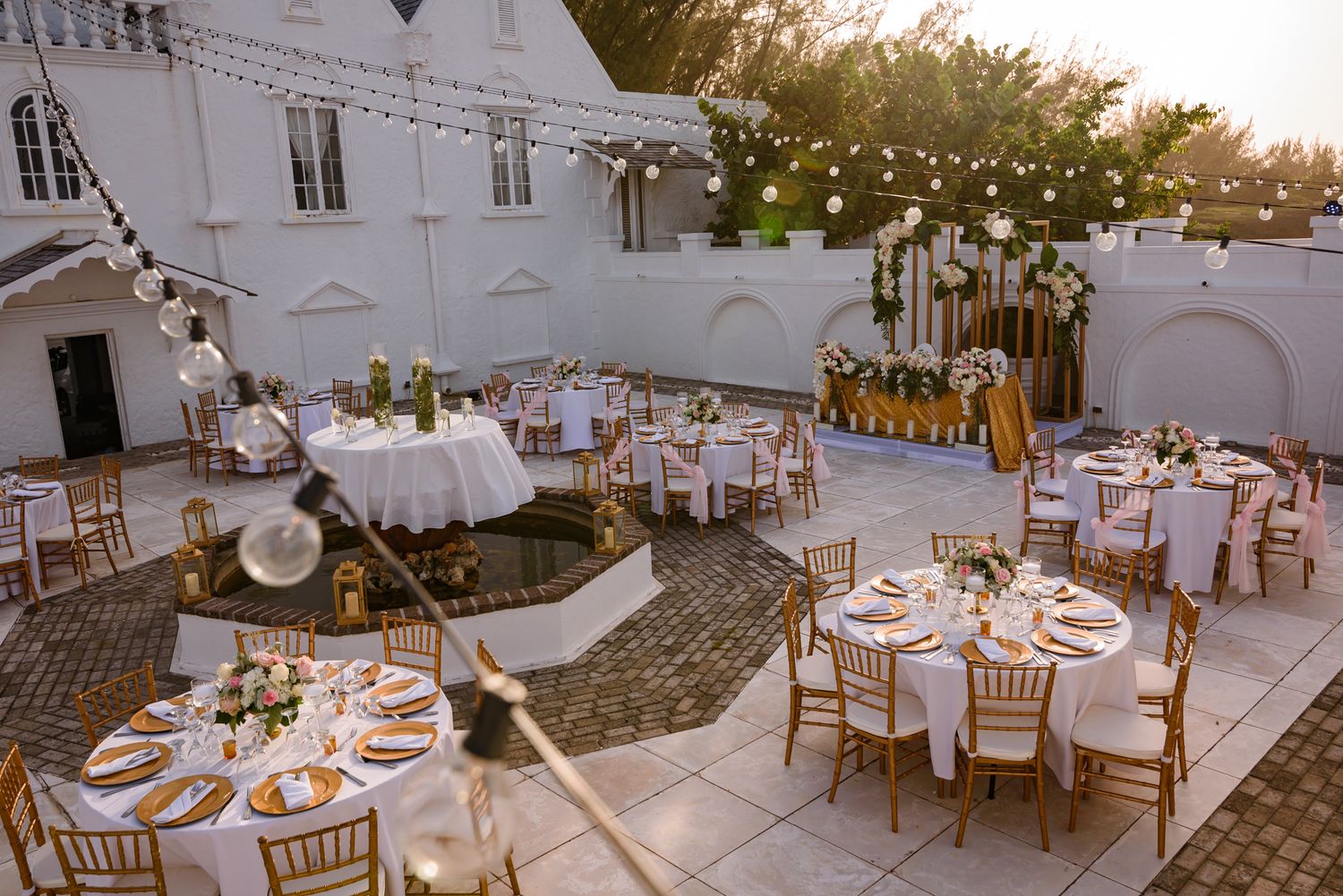 Panoramic view of outdoor wedding reception with string lights and round tables.