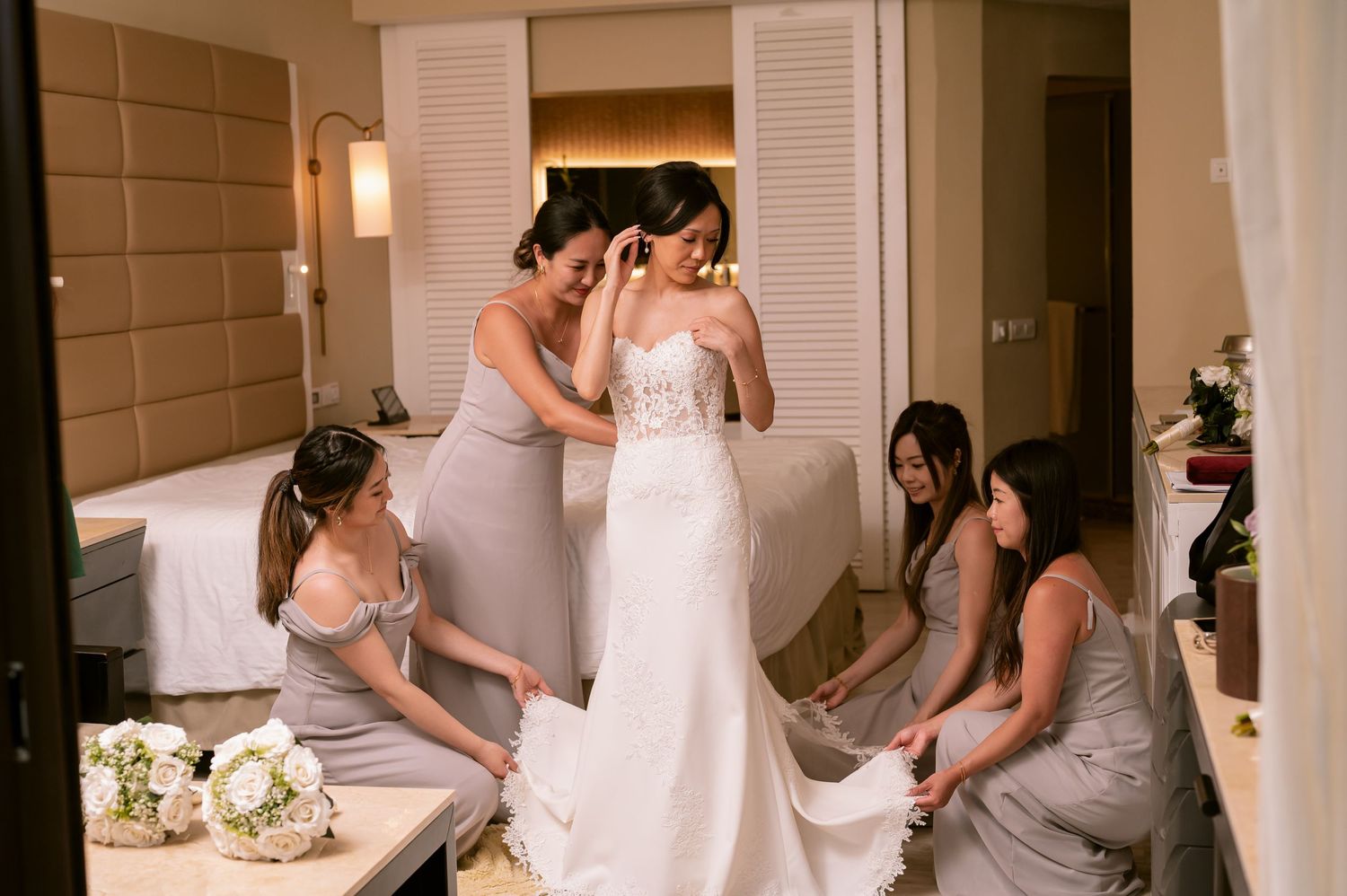 Bridesmaids helping with wedding dress preparations in an elegant room.