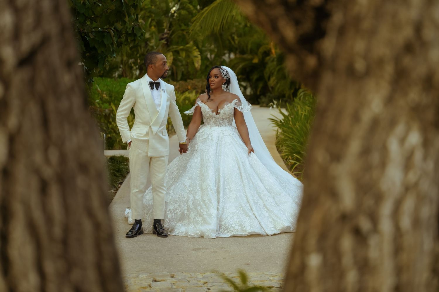 Garden wedding portrait through trees featuring elegant white attire.