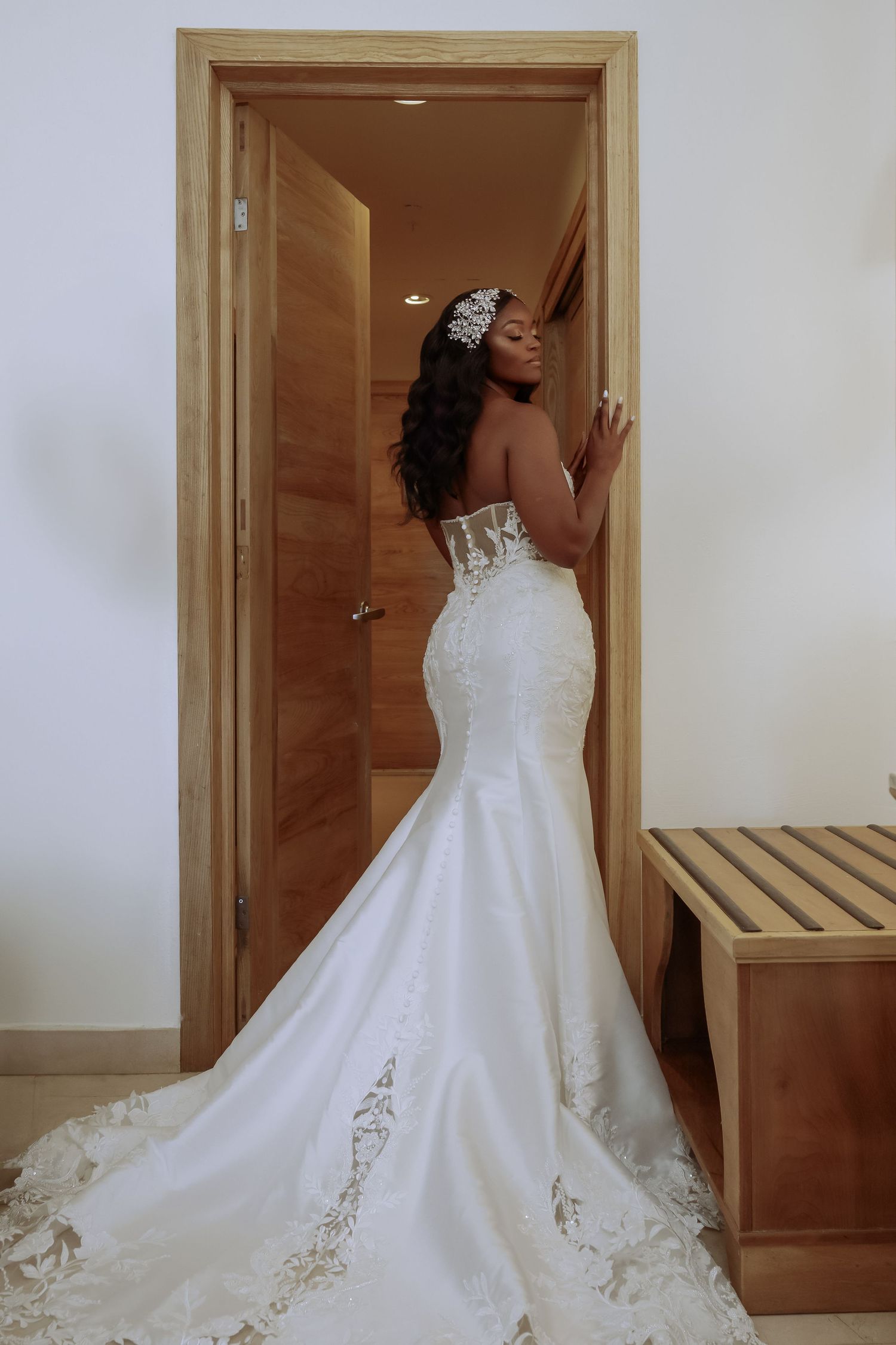 Elegant white wedding dress with lace details and long train displayed in a dressing room.